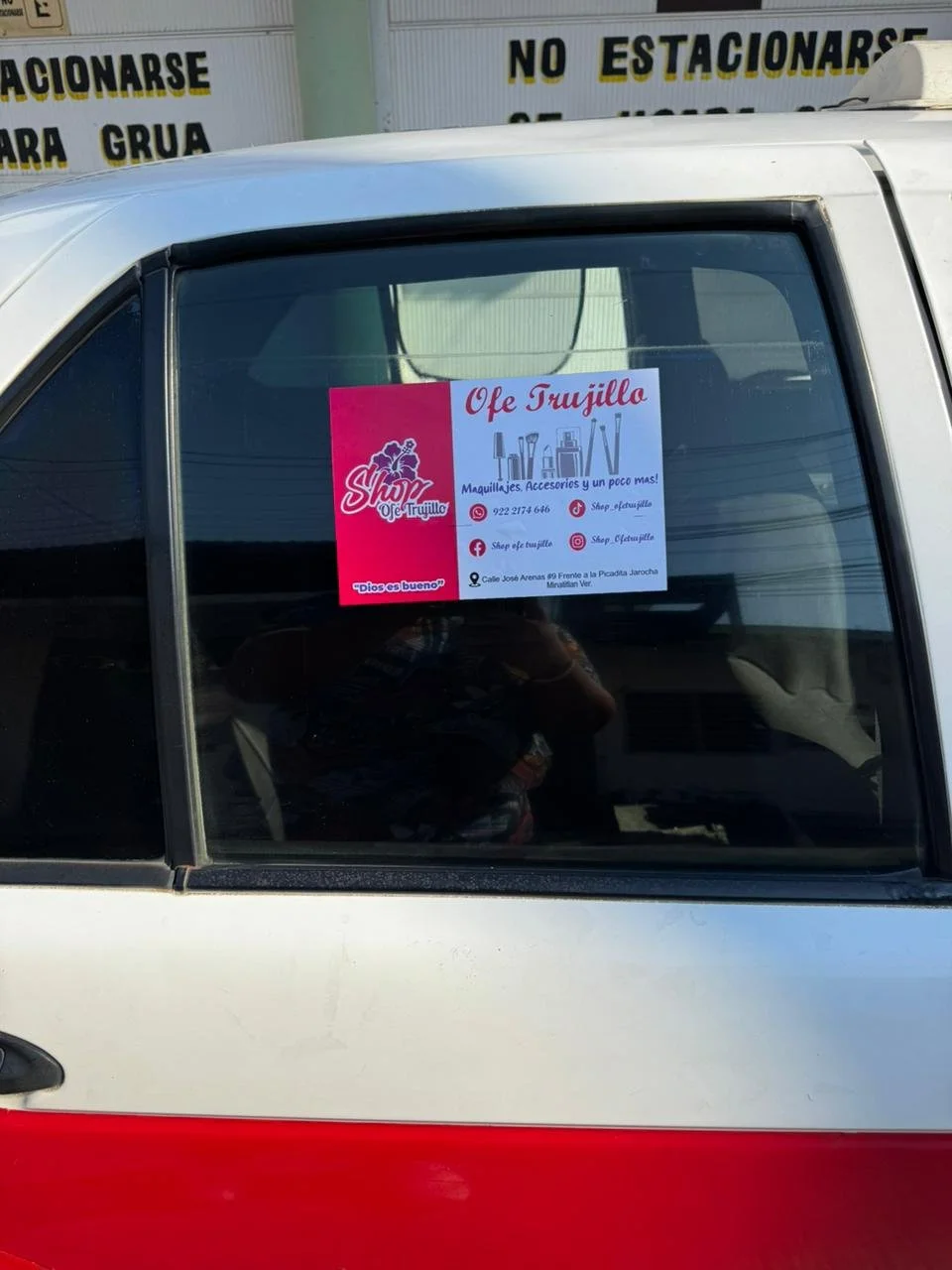 Publicidad en la ventana de un vehículo para una tienda de maquillaje, accesorios y más llamada Shop Ole Trujillo, con contacto en redes sociales y dirección.