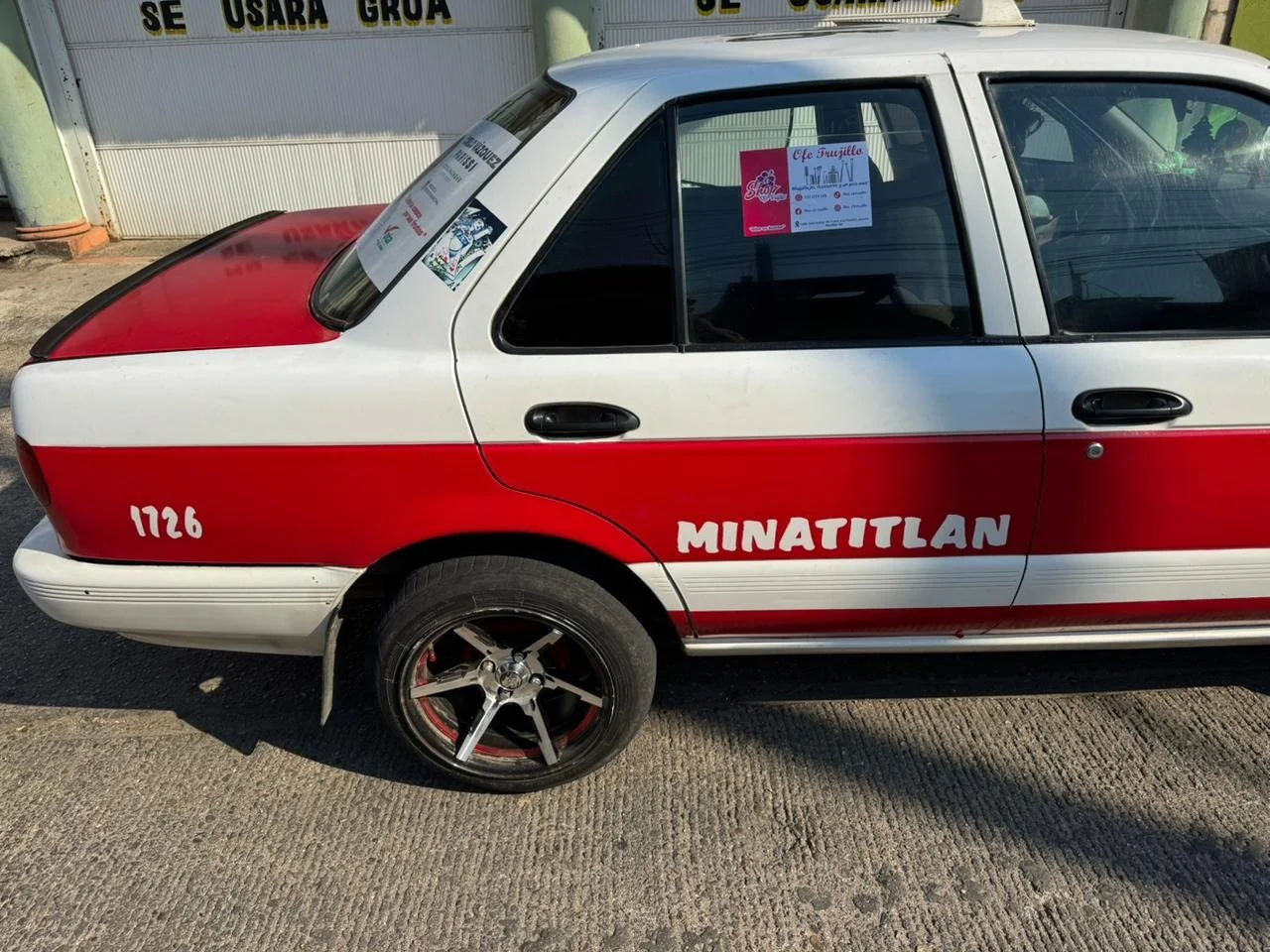 Auto de color blanco y rojo con la palabra MINATITLAN en el costado, número 1726 y un cartel en la ventana que dice 'Ole Muñito'