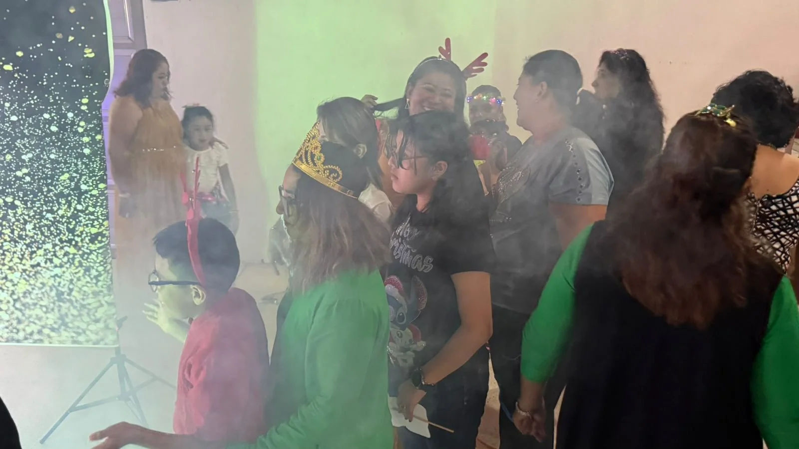 Grupo de personas celebrando en una fiesta de Navidad, algunas con gorros navideños, en un ambiente festivo y con niebla o humo en el aire.