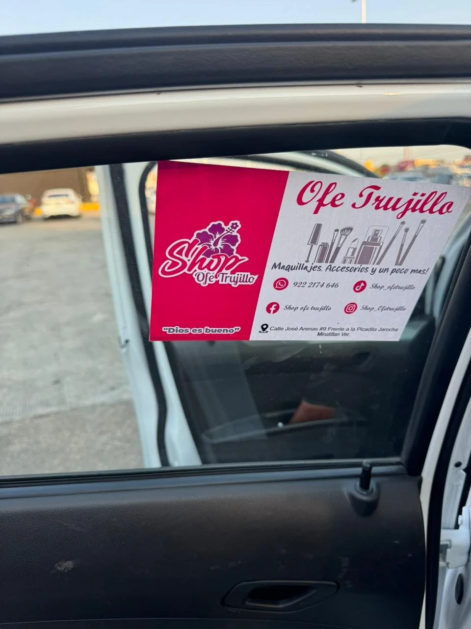 Publicidad de una tienda llamada Shop Ofe Trujillo en la ventana de un carro, que oferta maquillaje, accesorios y más