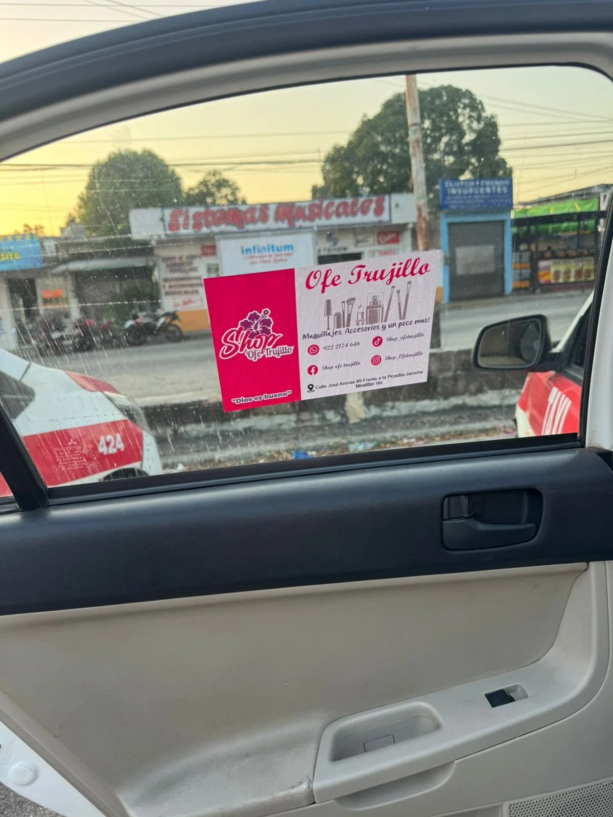 Publicidad de la tienda de artículos de belleza y maquillajes 'Ofe Trujillo' en la ventana de un vehículo, con dirección y contacto, además de sus redes sociales y ubicación en la calle José Arenas.
