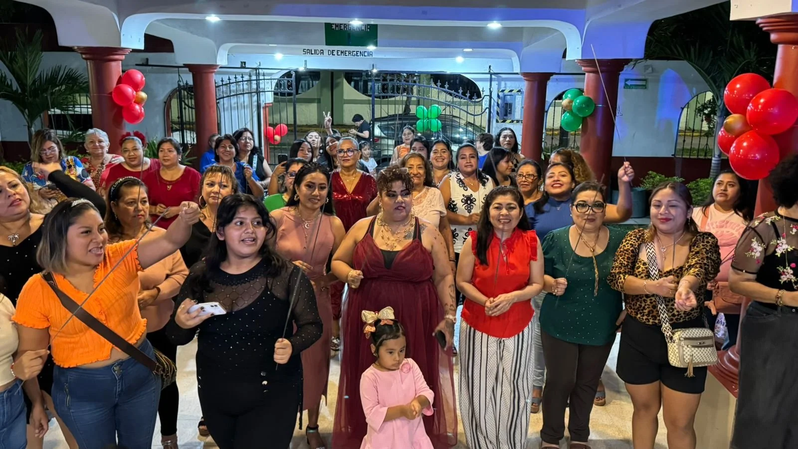 Grupo de personas celebrando en un lugar decorado con globos de colores, algunas personas están sonriendo y levantando las manos.