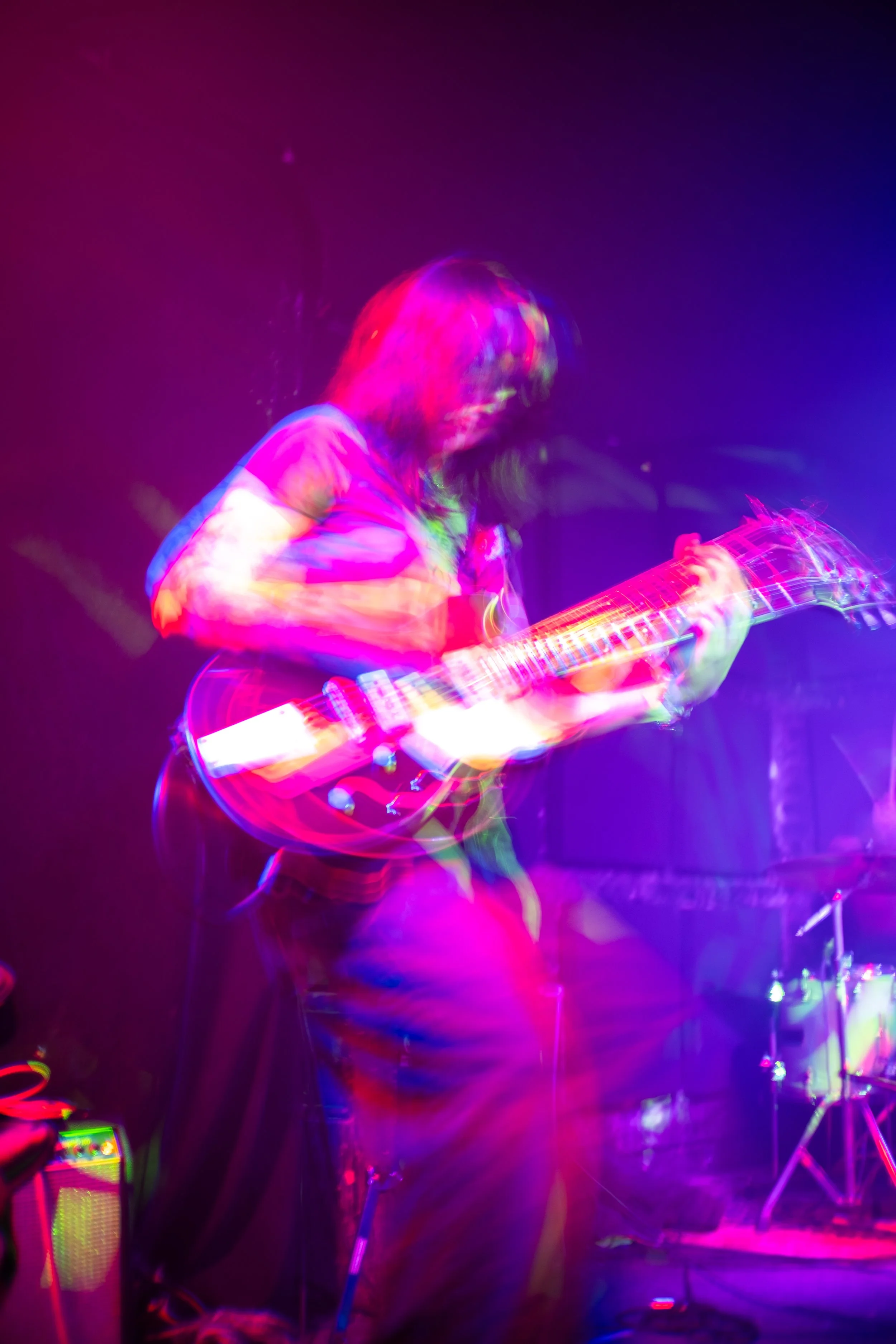 Blurred image of a person playing an electric guitar with colorful stage lights.