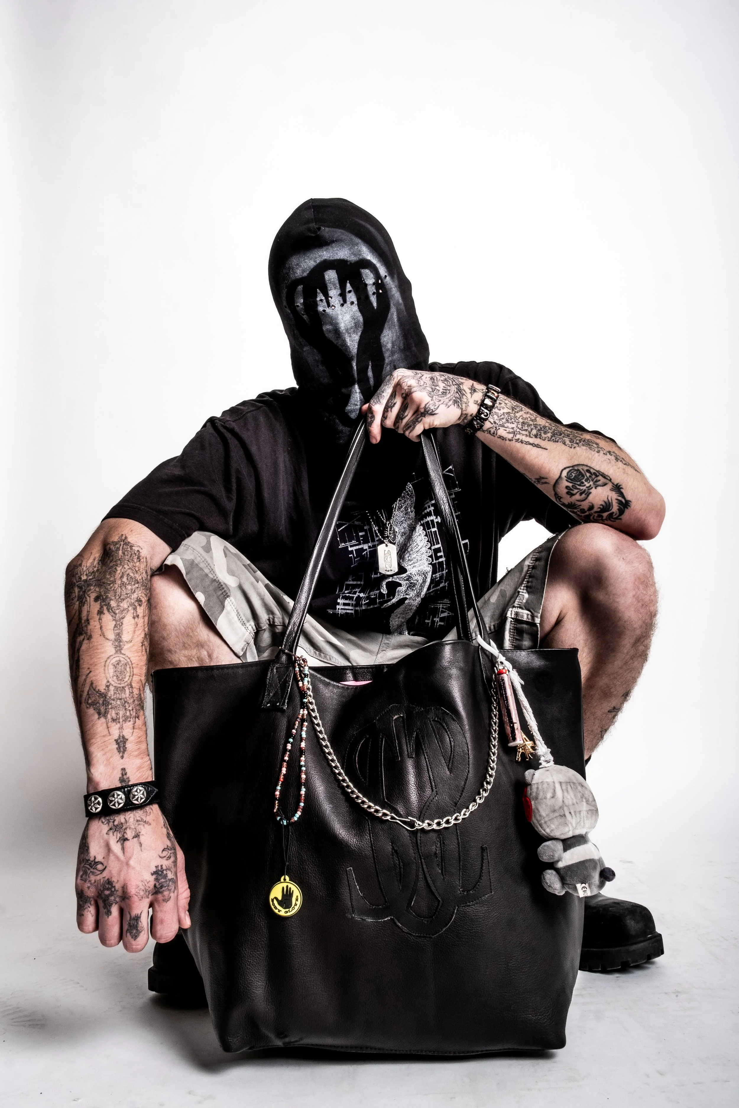 Person wearing a mask holding a large black bag with tattoos on arms