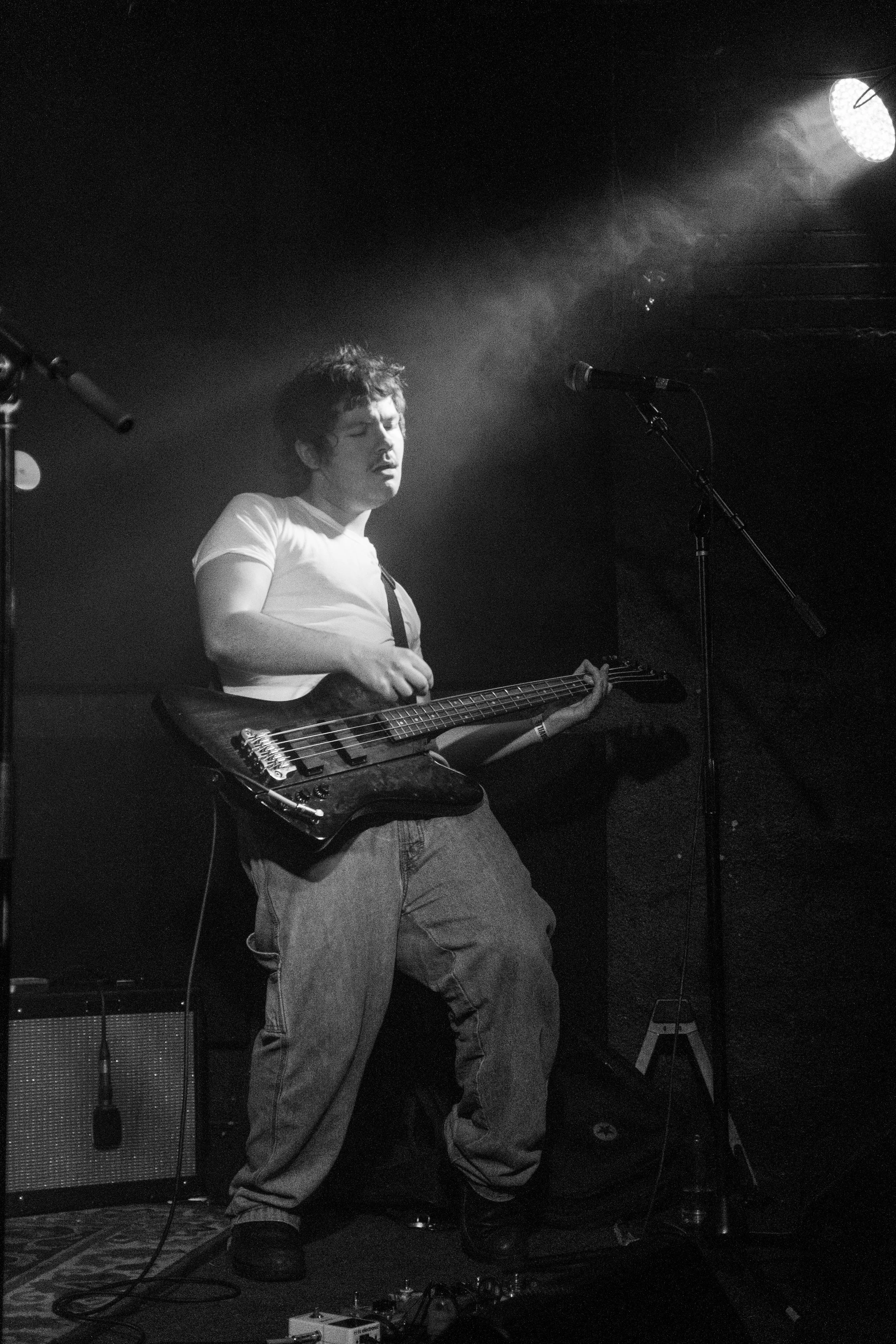 Black and white photo of a musician playing a guitar on stage with a microphone and spotlight.