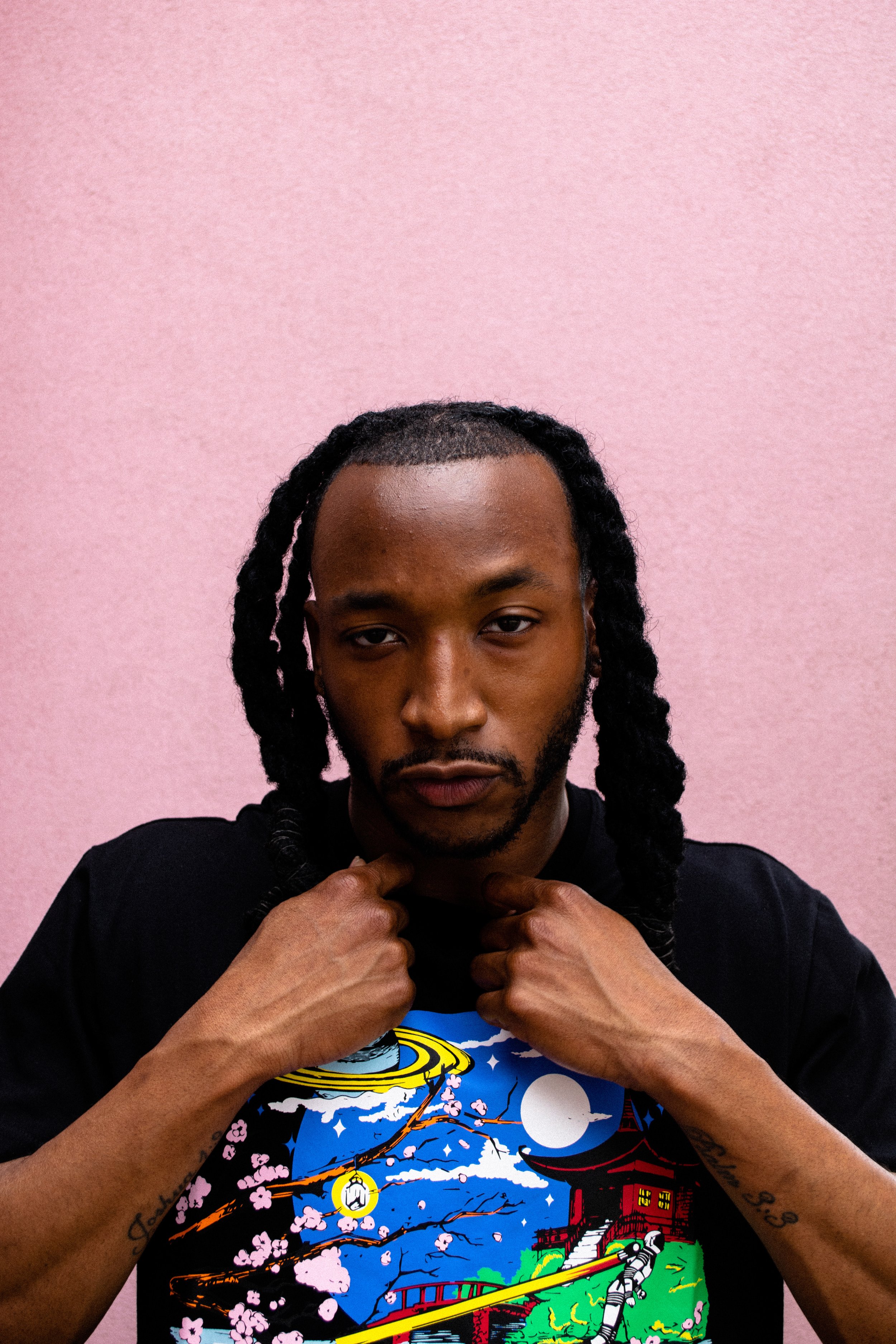 Person with braided hair and graphic t-shirt standing against a pink background.
