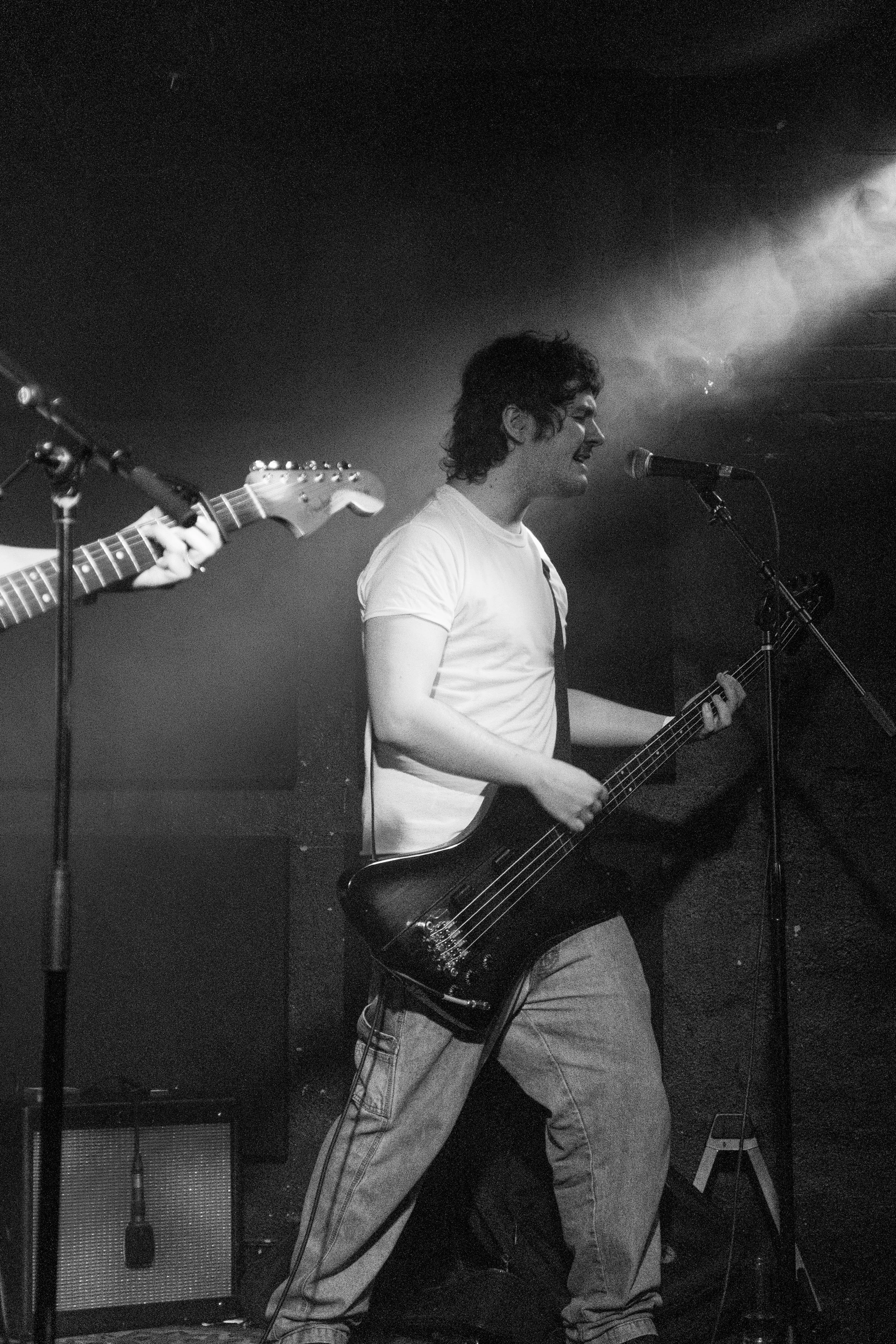 Musician playing bass guitar on stage in black and white photography.