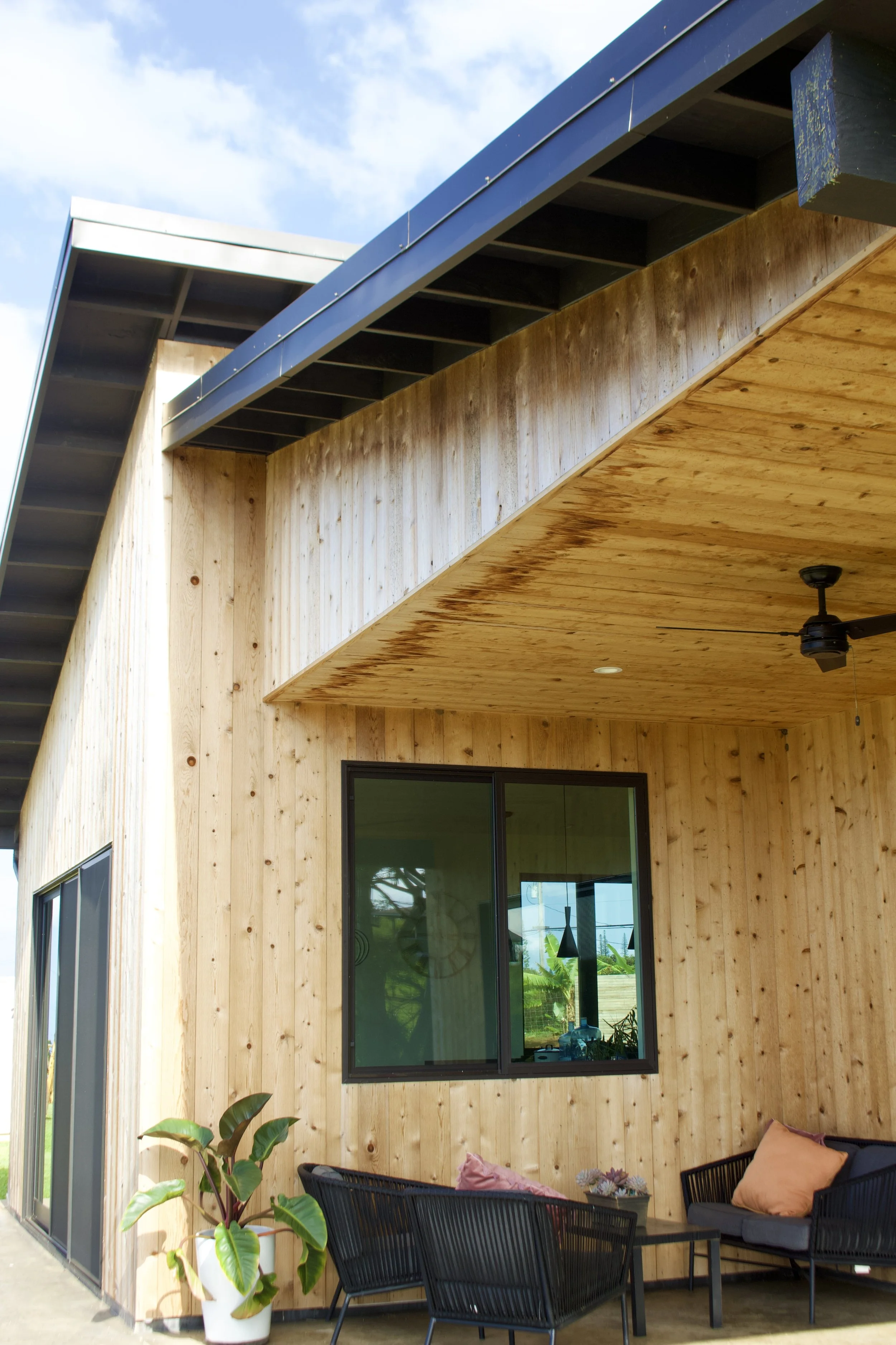 Modern house exterior with wooden paneling, a window, and a patio with black furniture and cushions.