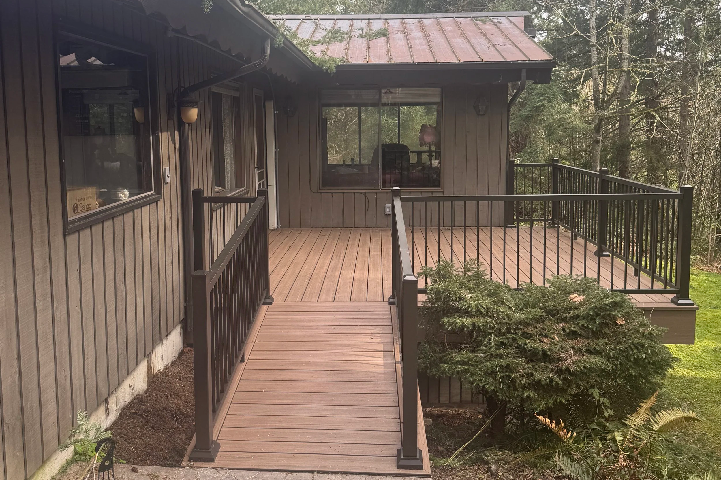 A wooden deck attached to a house with black railing, surrounded by trees and greenery.