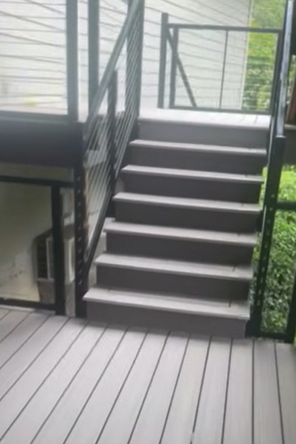 Outdoor staircase leading up to a screened porch with a metal railing, with greenery visible in the background.