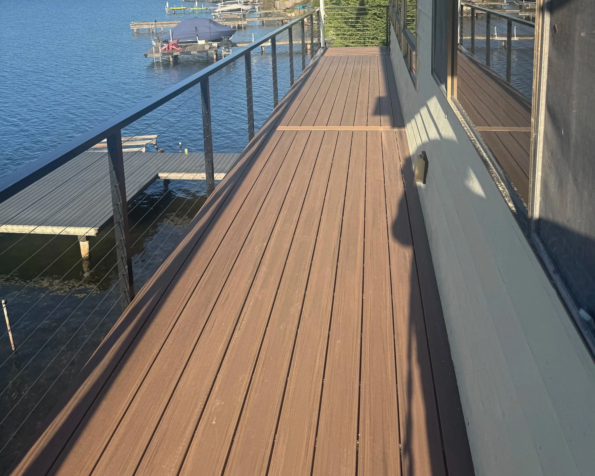 A wooden deck balcony overlooking a body of water with docked boats and a floating dock with chairs and an umbrella.