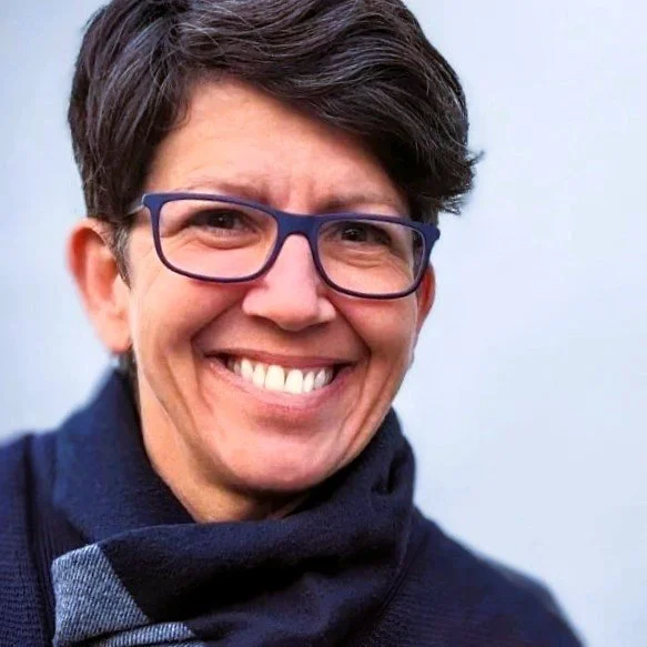Smiling woman wearing dark rectangular glasses and a black scarf