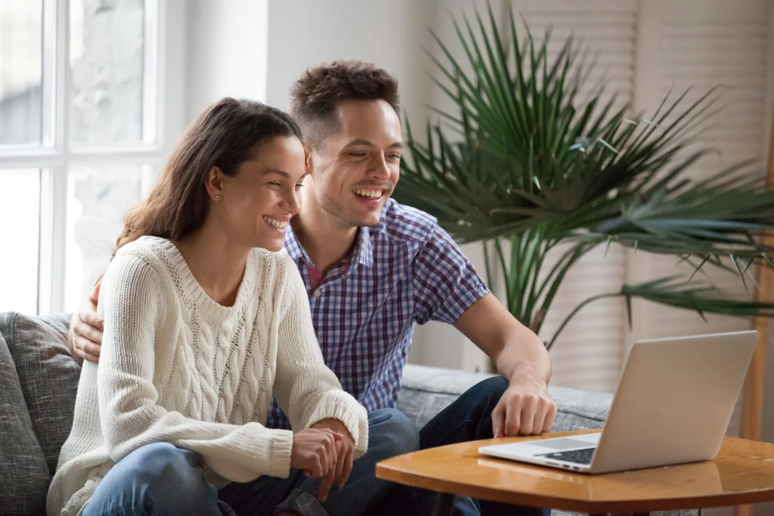 Smiling couple sitting on a couch, looking at a laptop.