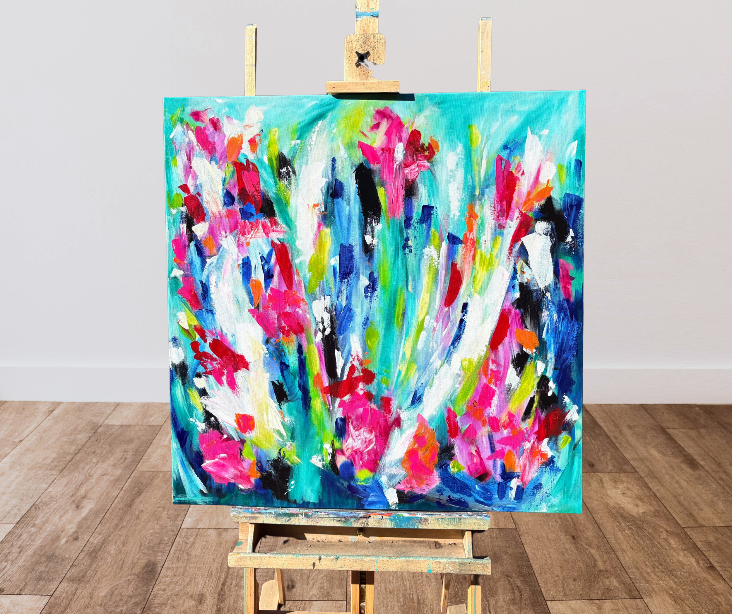 An abstract colorful painting on an easel in front of a plain wall and hardwood floor.