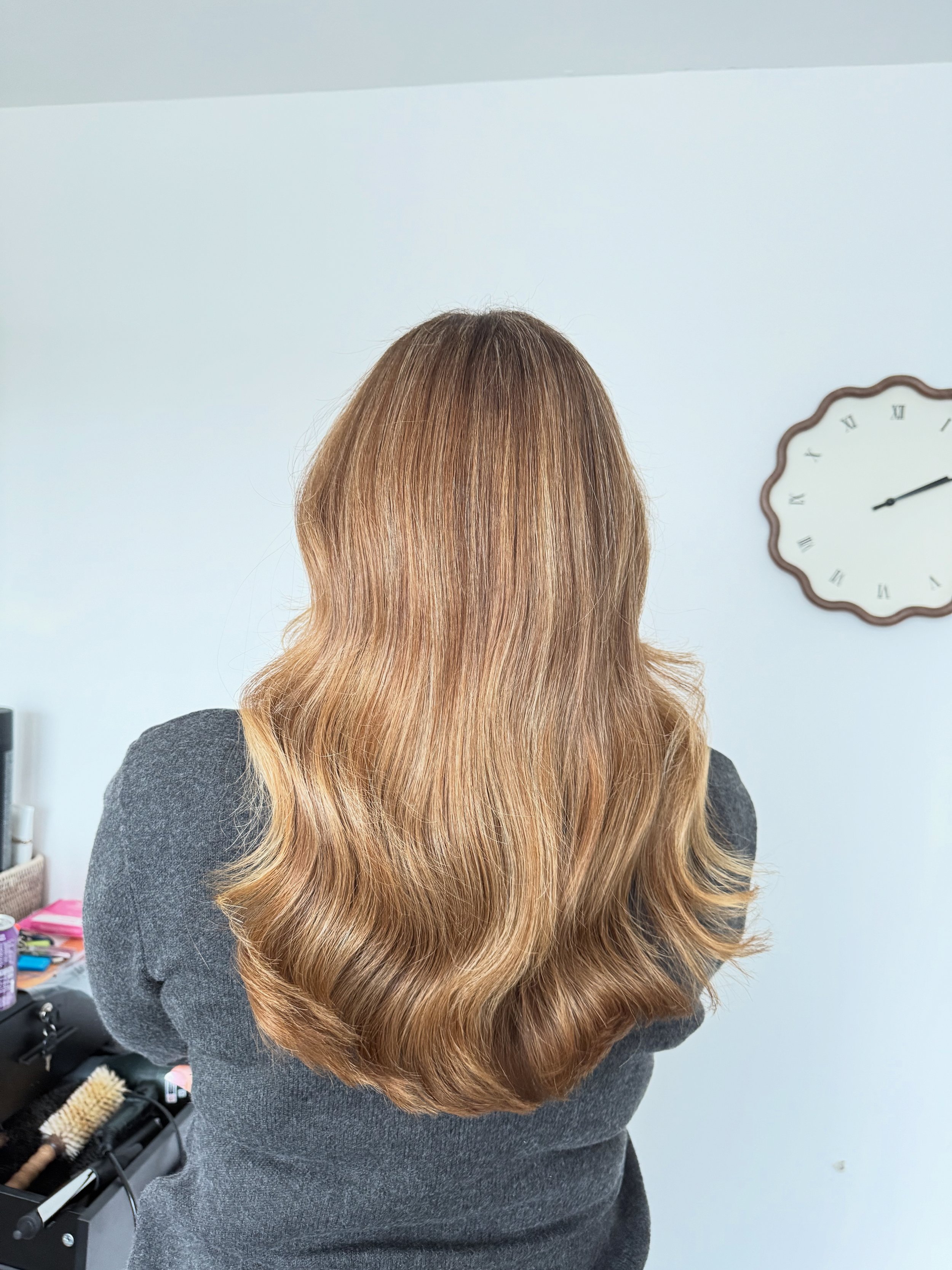 Back view of a woman with long, wavy, brown hair standing in a salon or similar space.