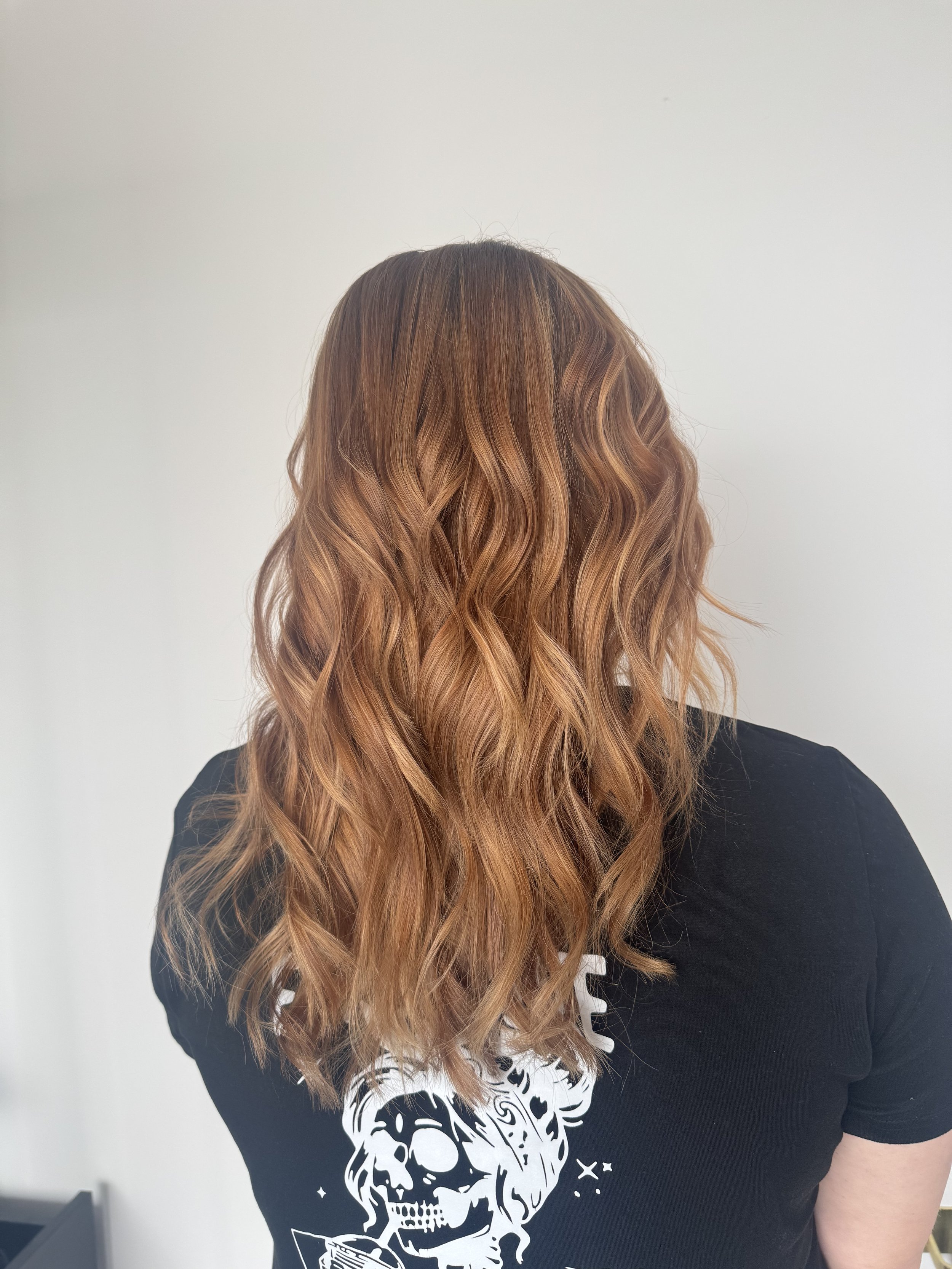 Back of woman's head showing wavy, reddish-brown hair, wearing a black T-shirt with a white skull design.