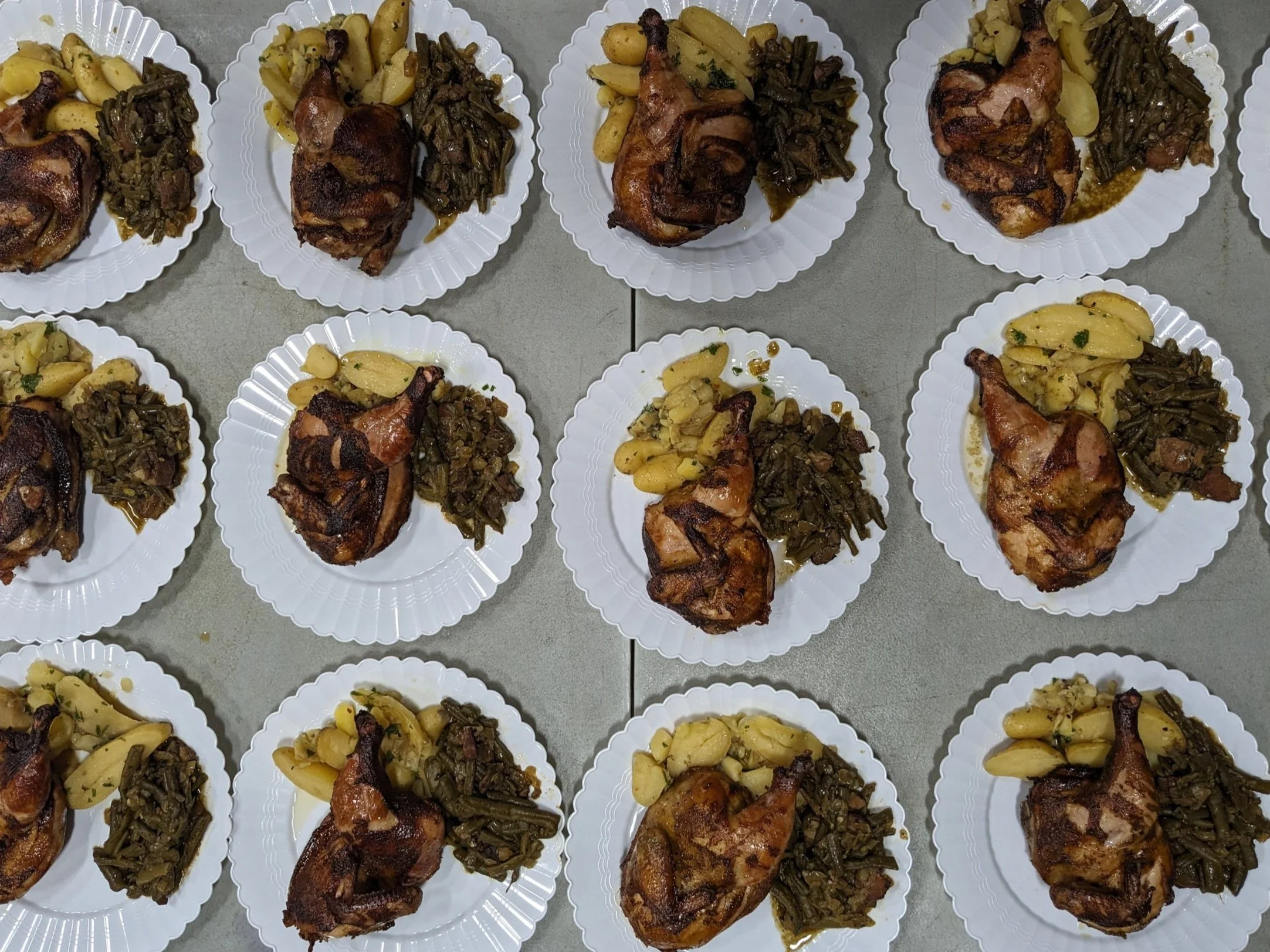 Multiple plates with cooked chicken legs, cooked greens, and garlic cloves.