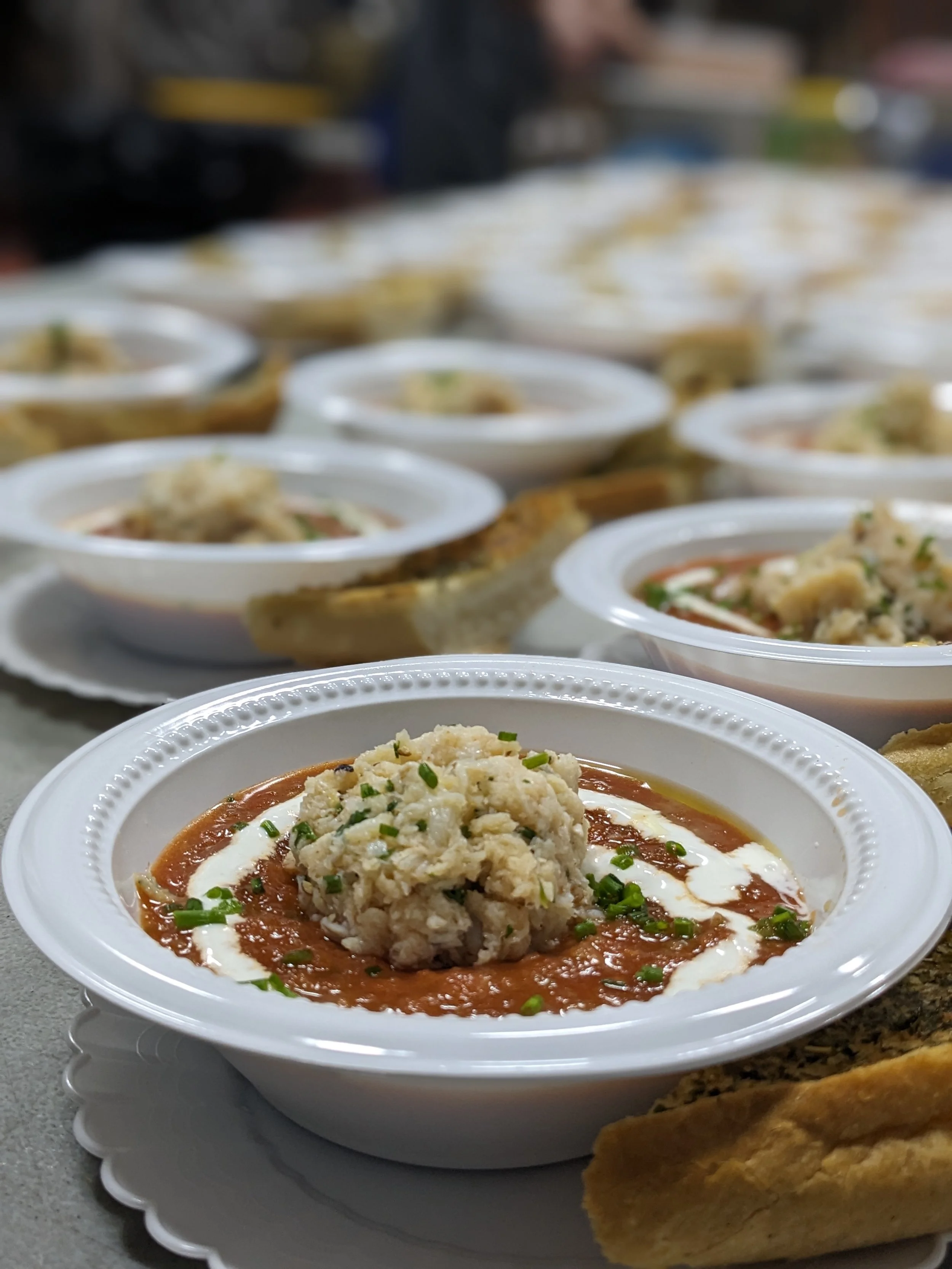 Multiple bowls of chili topped with cheese and chives, served with breadsticks, on a counter in a restaurant or food service setting.
