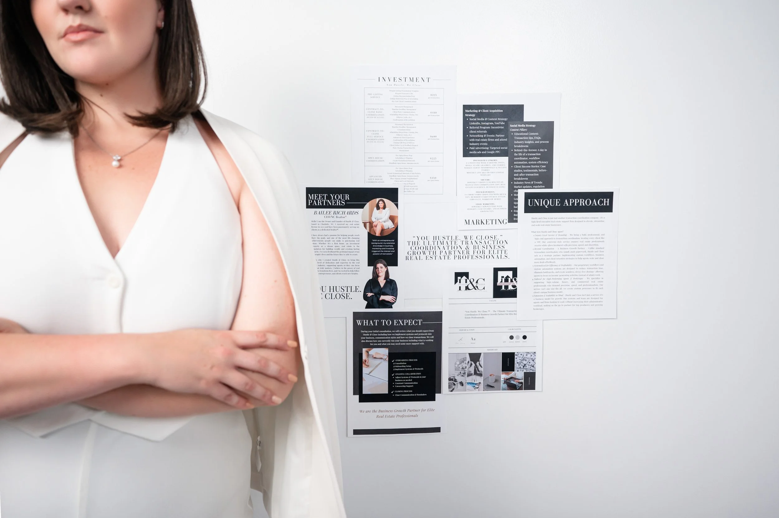 Part of a woman in a white sleeveless blazer with crossed arms standing in front of a wall with various business flyers and documents.