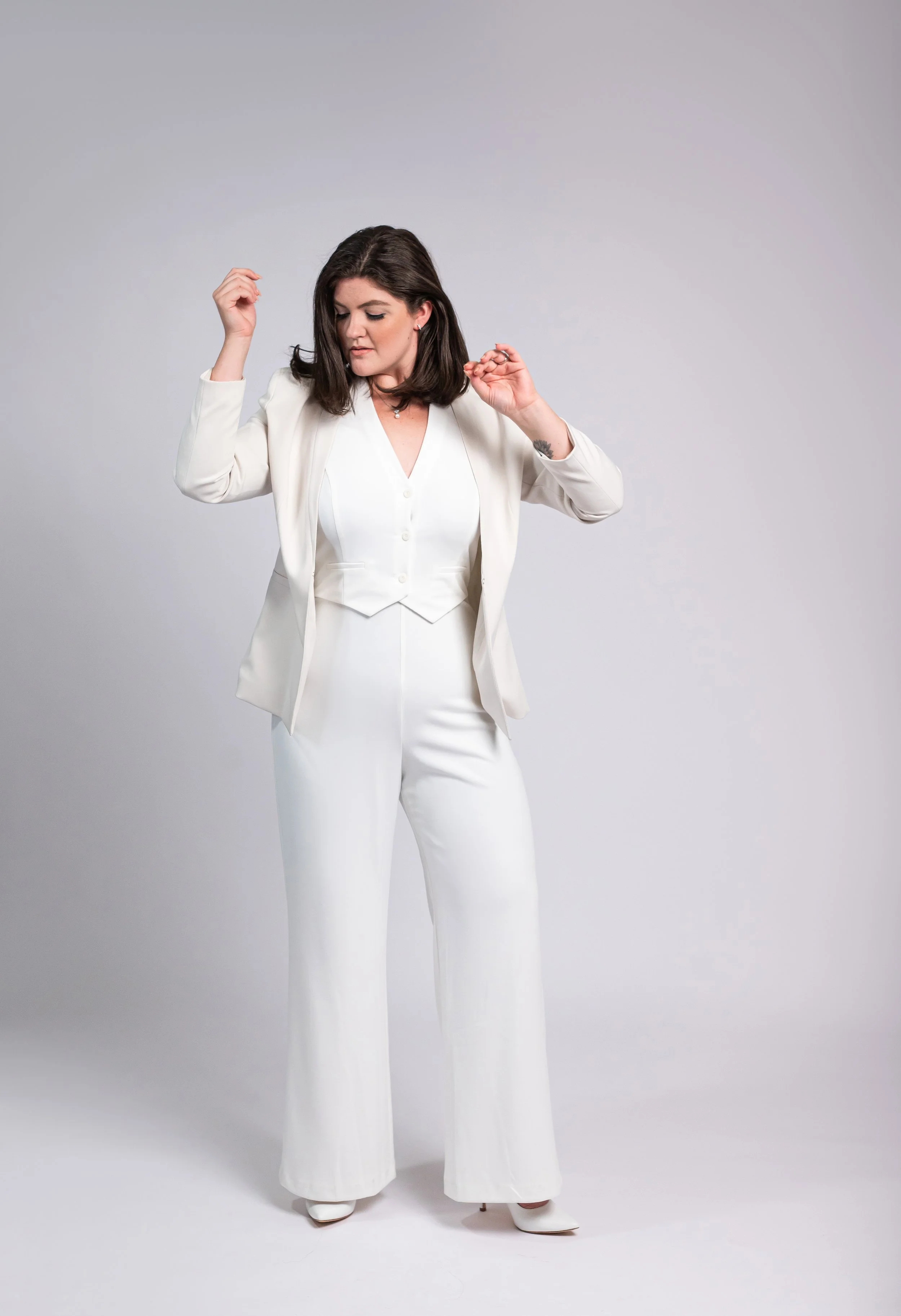 Woman in a white suit dancing against a plain background.