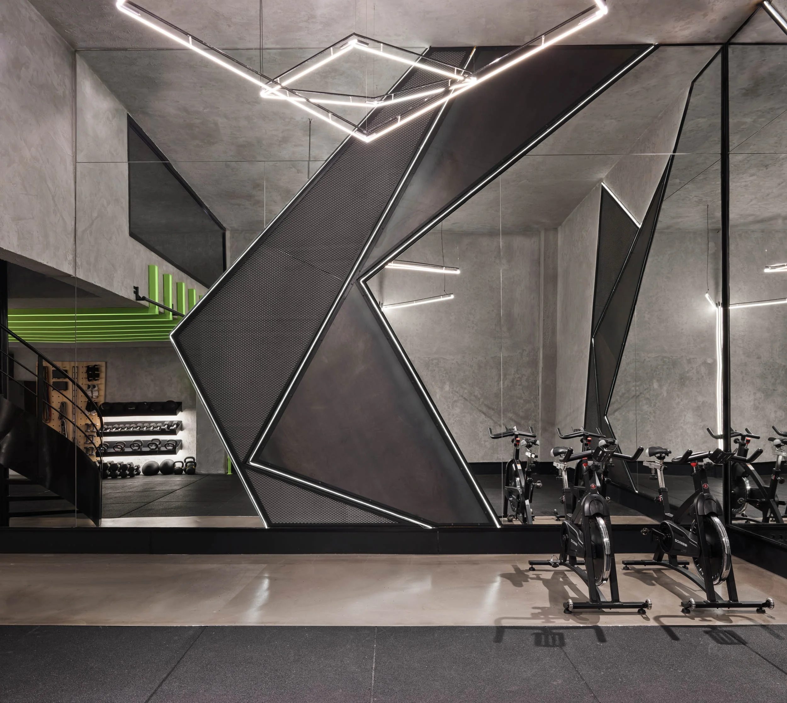 Modern gym with stationary bikes in front of geometric mirror installation and workout equipment in the background.