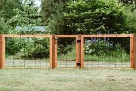 A wooden fence with two swinging gates in a backyard with trees and grass.