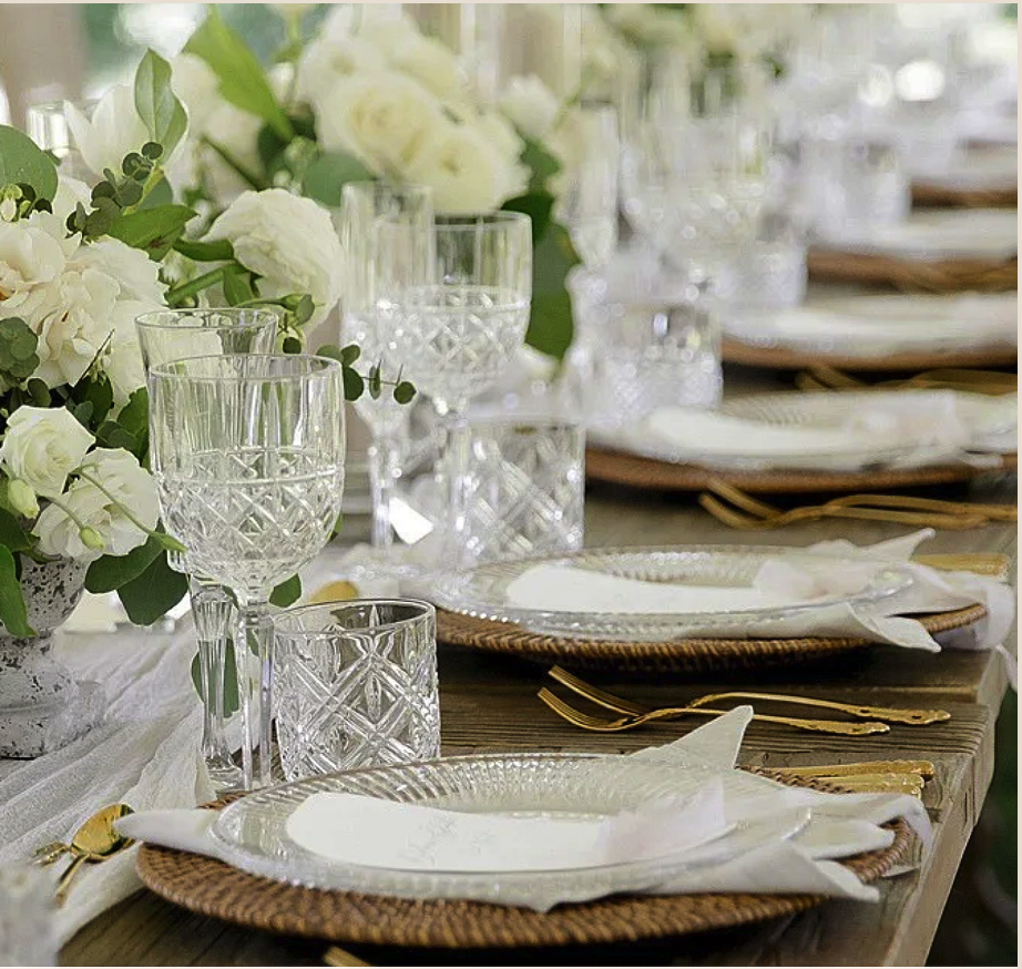 Elegant table setting with white plates, gold utensils, white napkins, crystal glasses, and a floral centerpiece of white flowers.