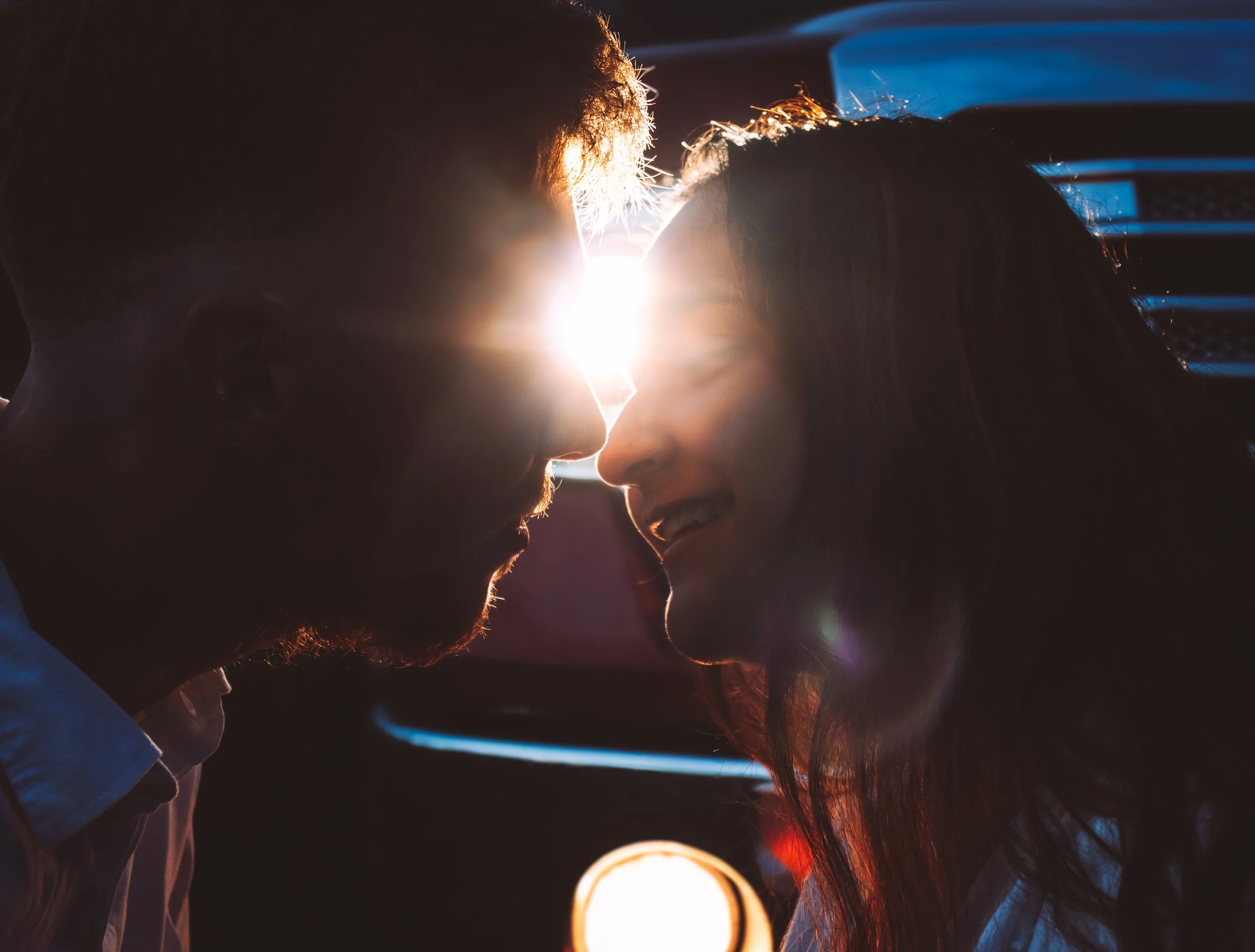 A close-up of a man and woman with their foreheads touching, backlit by bright sunlight, creating a silhouette.