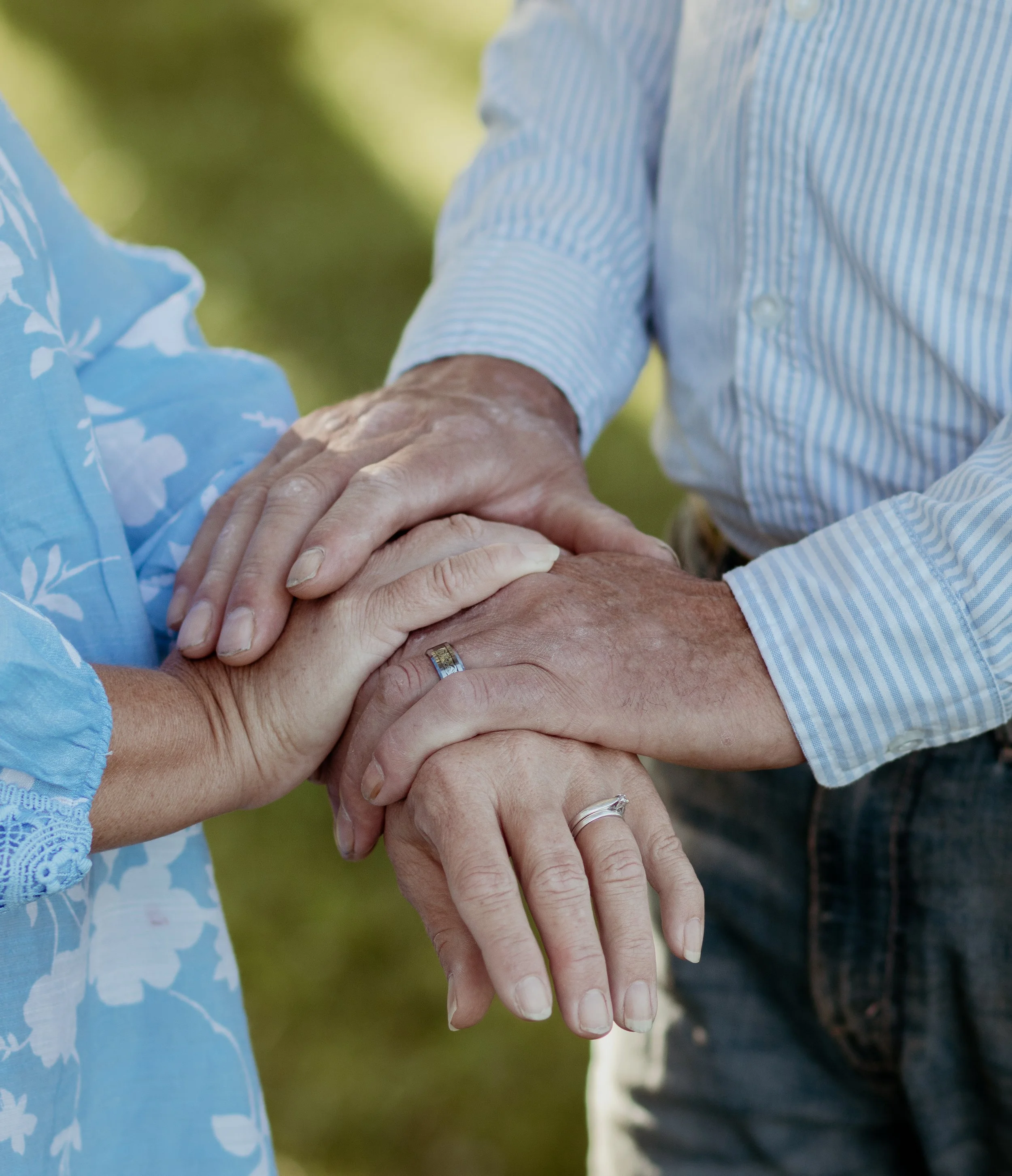 Multiple hands of older adults with rings touching in a heartfelt gesture outdoors.