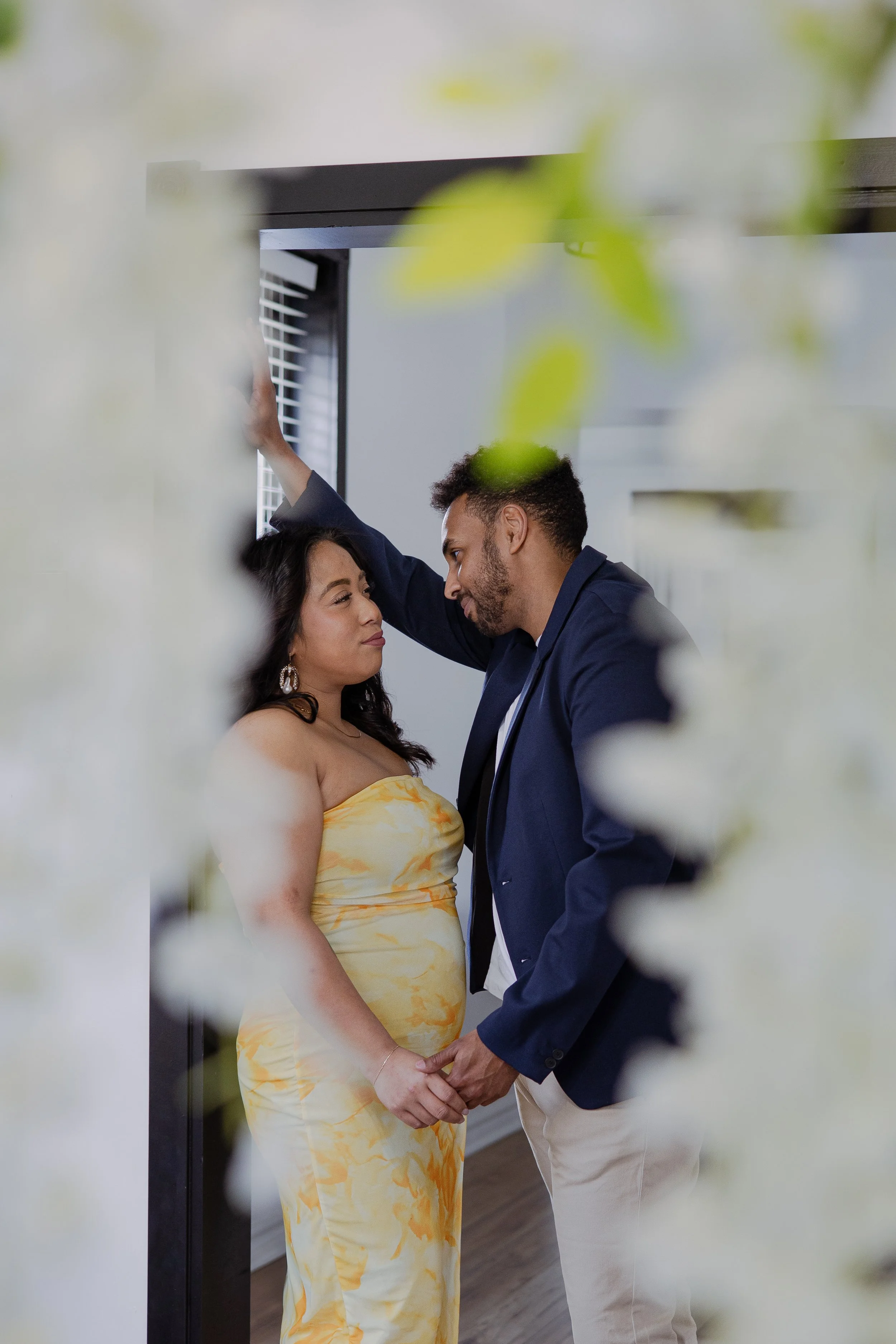 A couple holding hands and looking into each other's eyes during a wedding ceremony, with leaves and flowers blurred in the foreground.