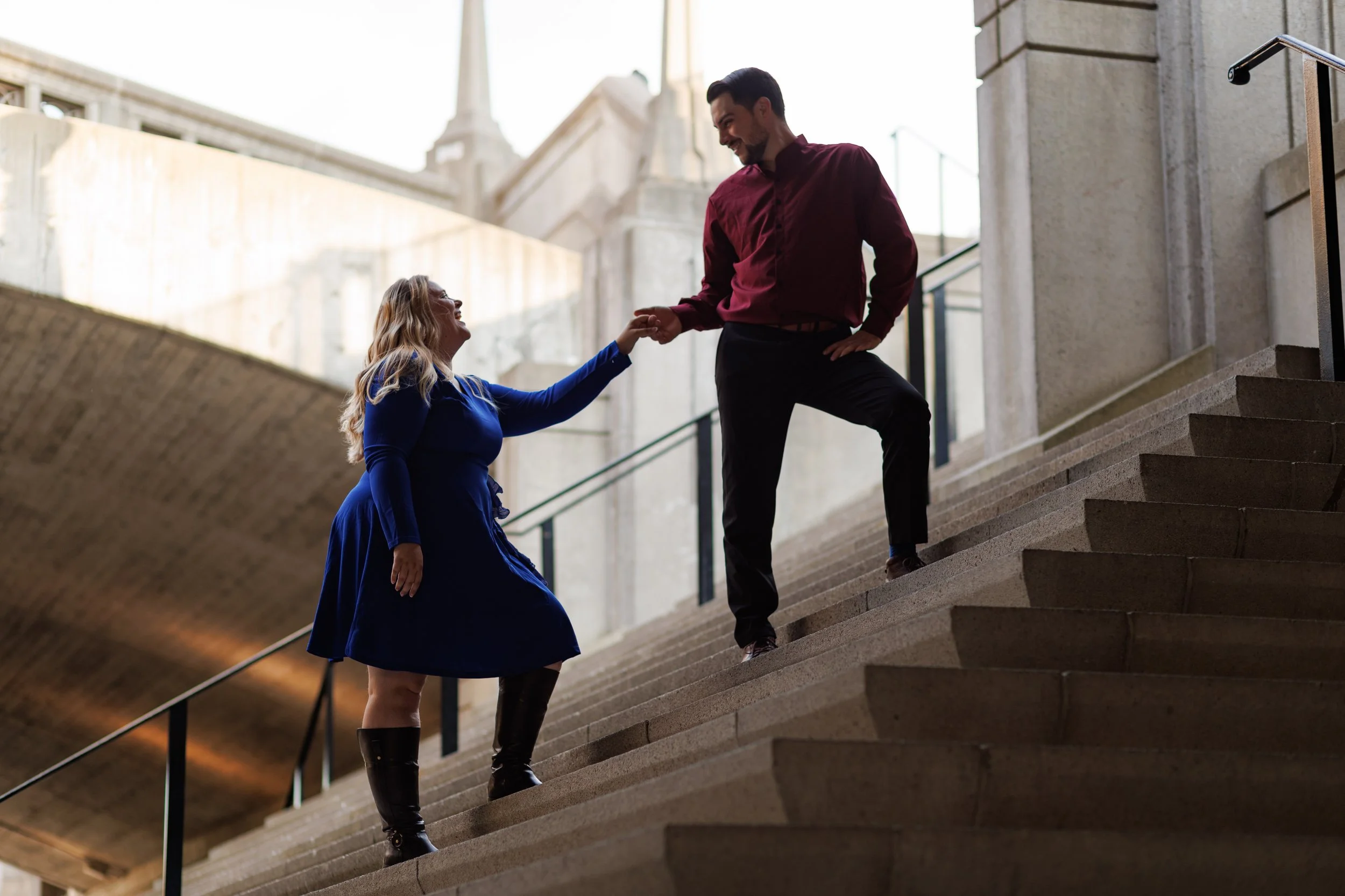 A man helping a woman up concrete stairs outside a building.