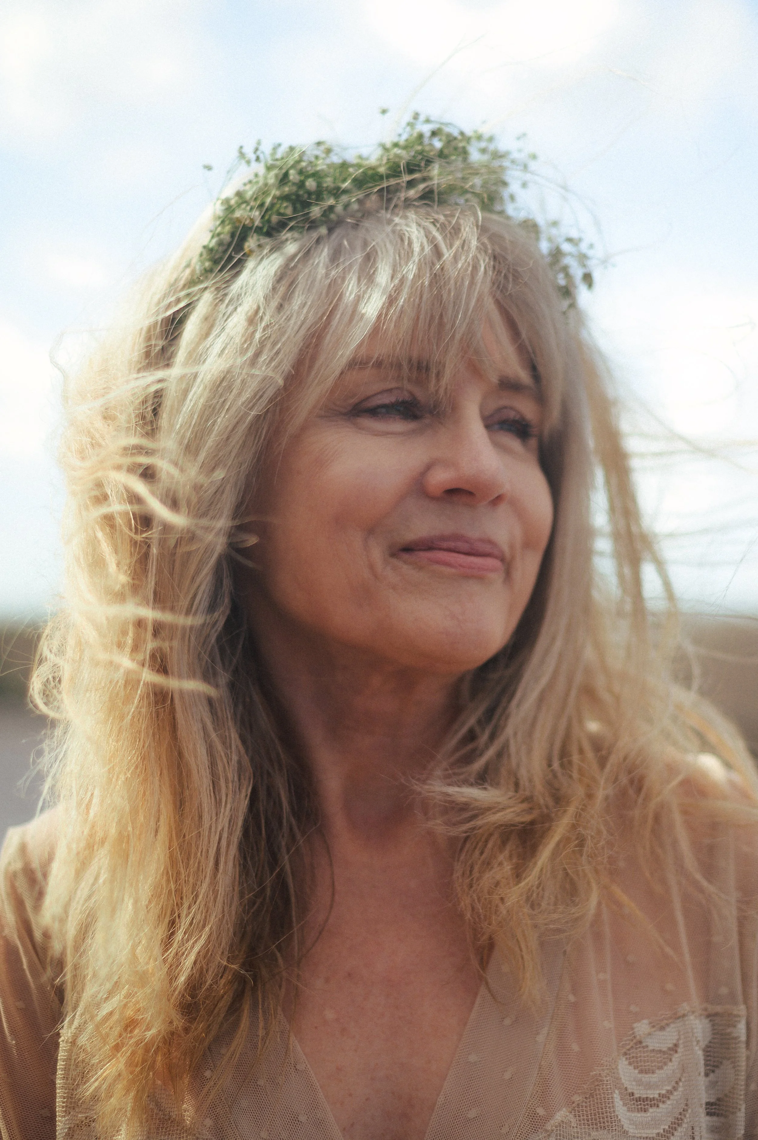 portrait of older blonde woman with hair blowing in the wind wearing flower crown photographed by black woman photographer in Newport News