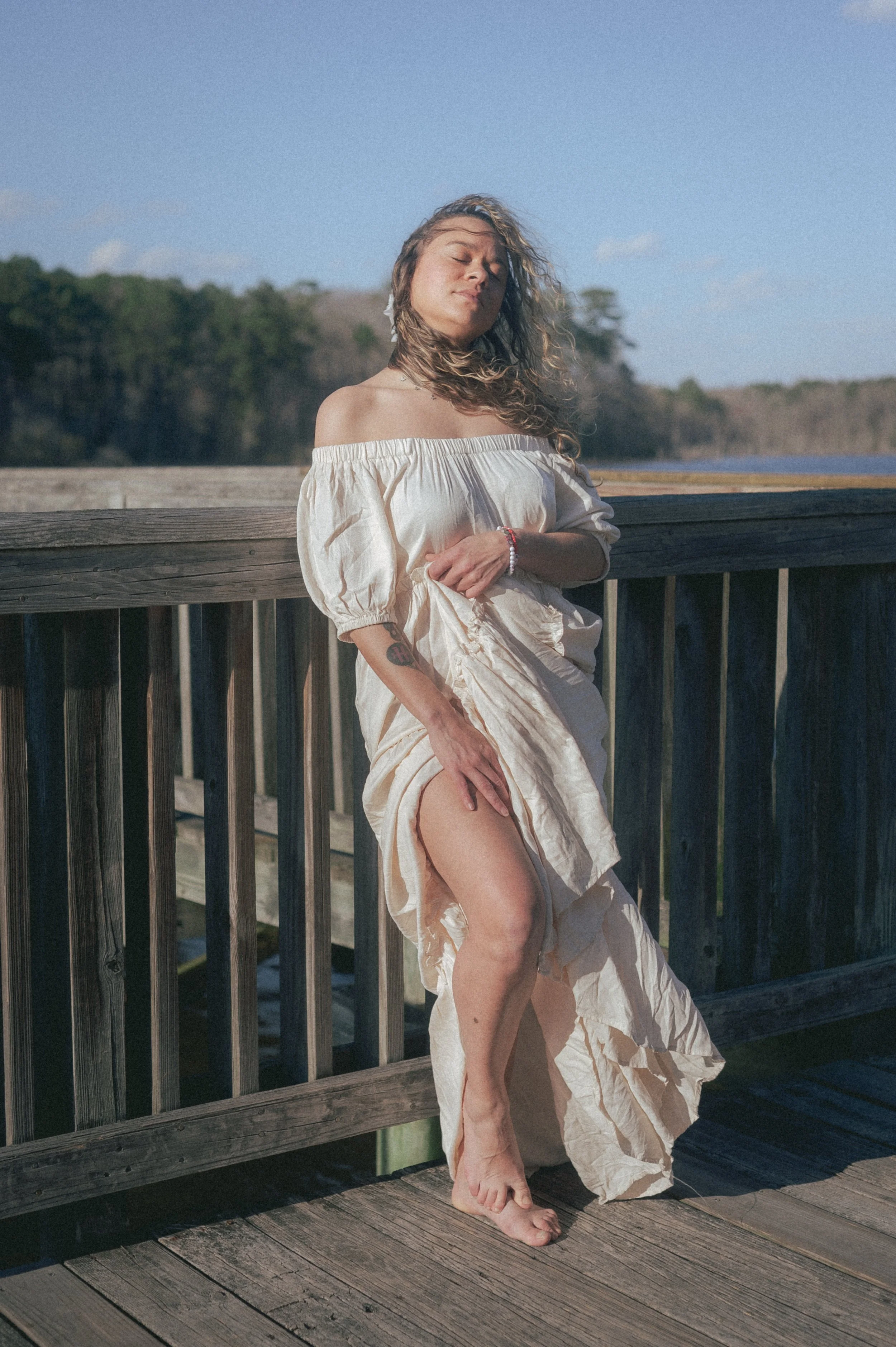 young woman posing in off shoulder peasant dress on wooden bridge photographed by black woman photographer in Newport News