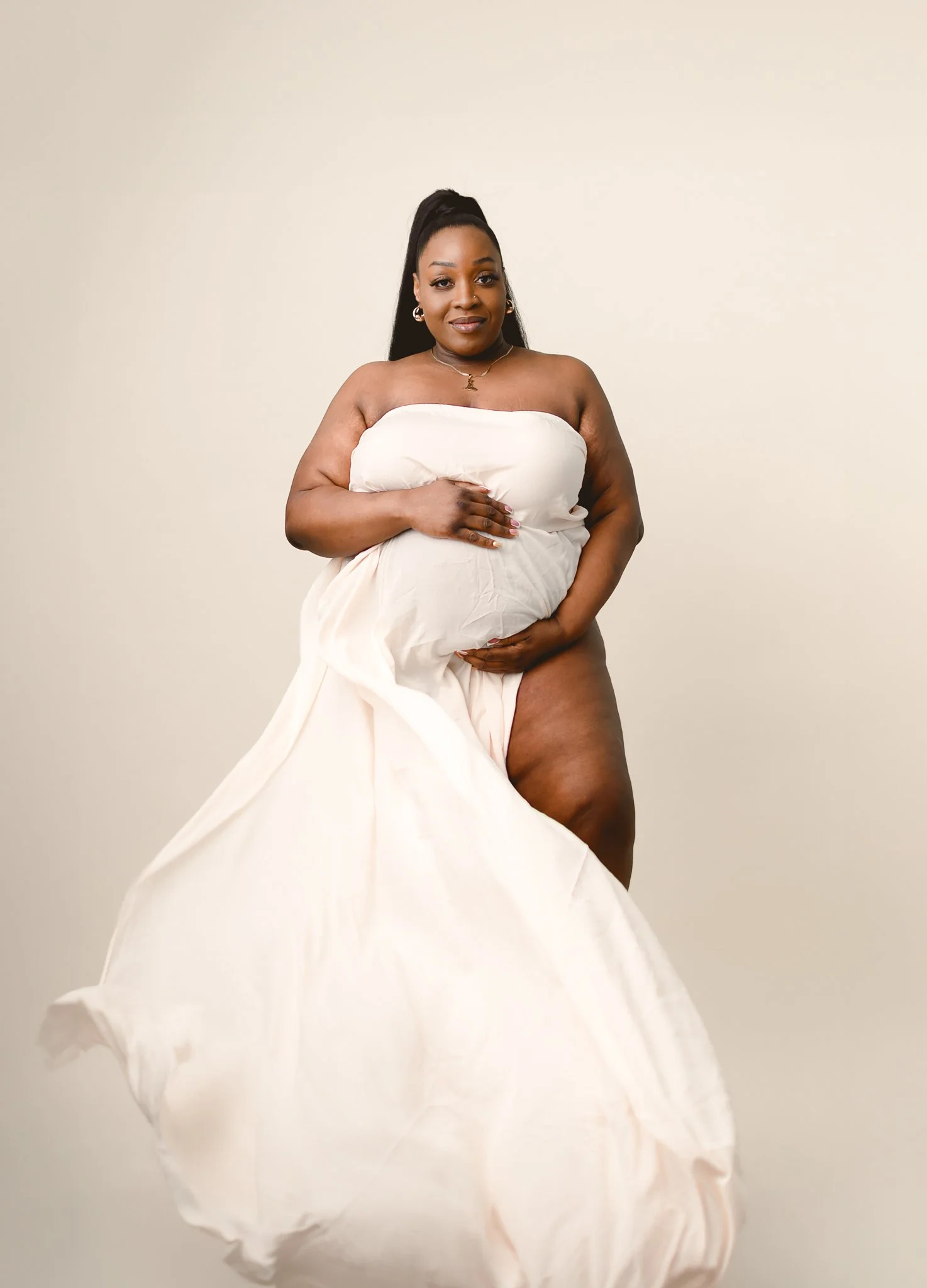 photo of plus size black woman posing for maternity photoshoot with flying dress and draped fabric. photo was taken by black woman maternity photographer in pontiac michigan photo studio