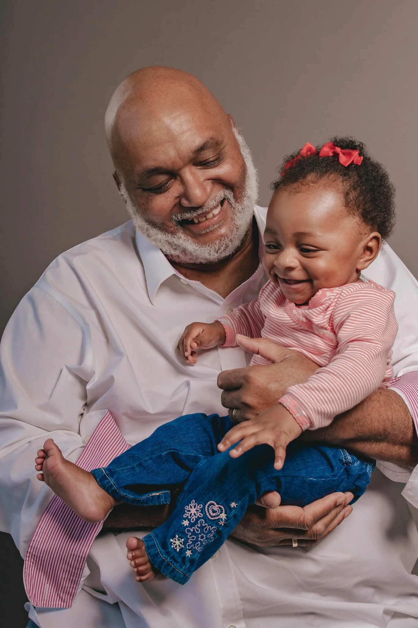 Photo of older black grandfather and black baby granddaughter laughing together. Grandfather is holding his grandchild in his arms. Photo was taken by black woman photographer in metro detroit area with a photo studio in pontiac, michigan.