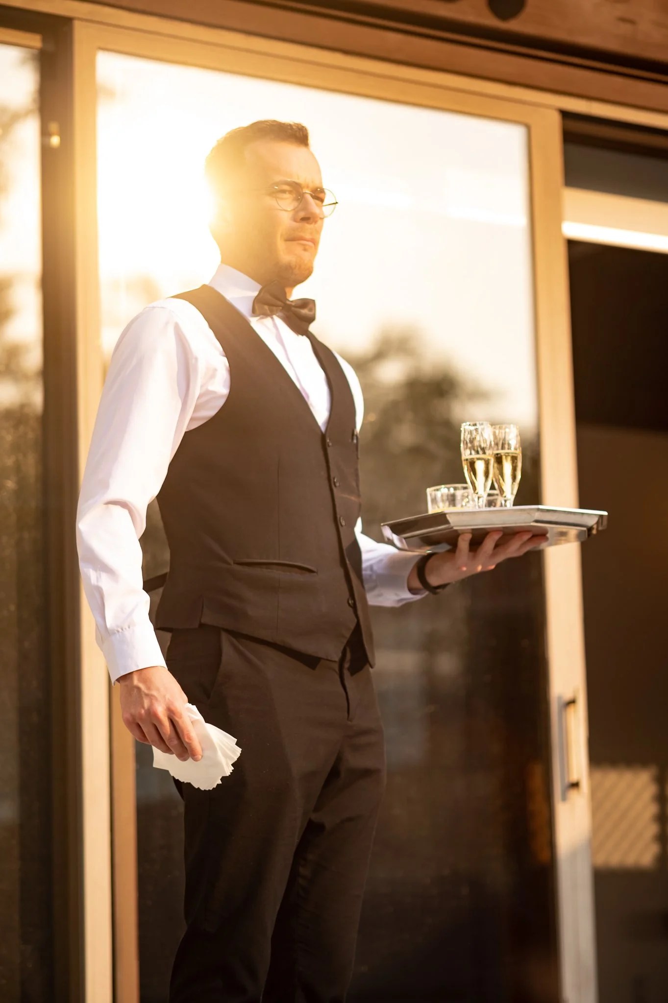 photo of waiter with sunset in backdrop while he holds a tray of champagne. photo taken by corporate event photographer in metro detroit michigan