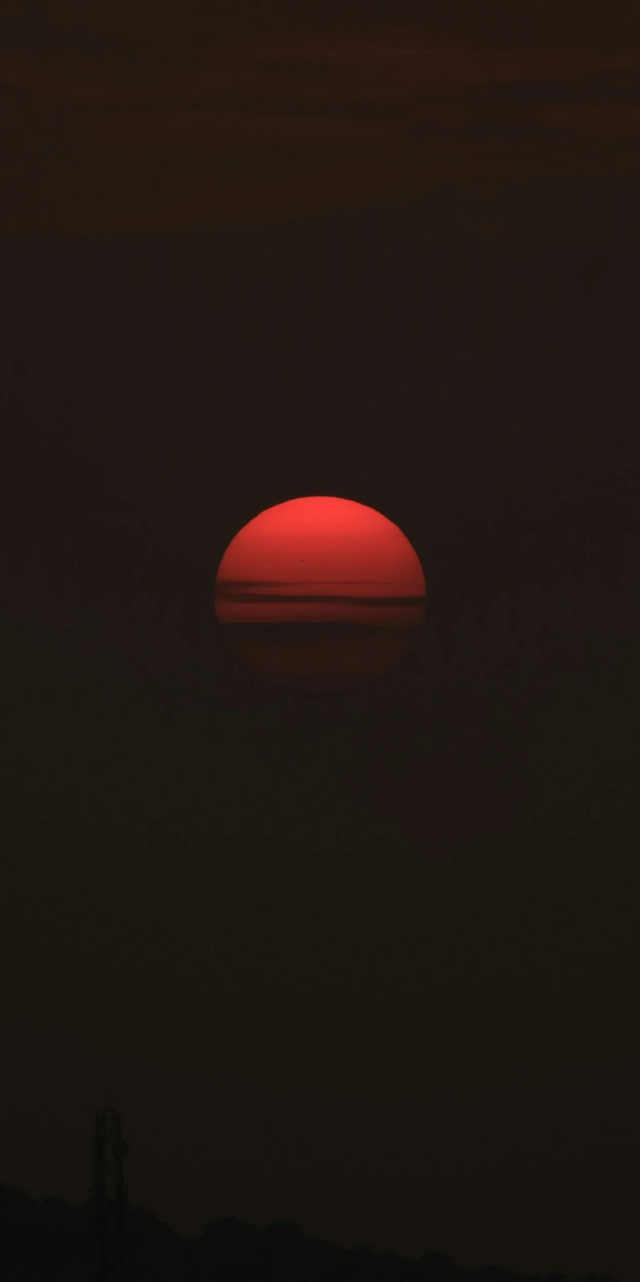 Sunset over a dark horizon with a red sun partially visible.