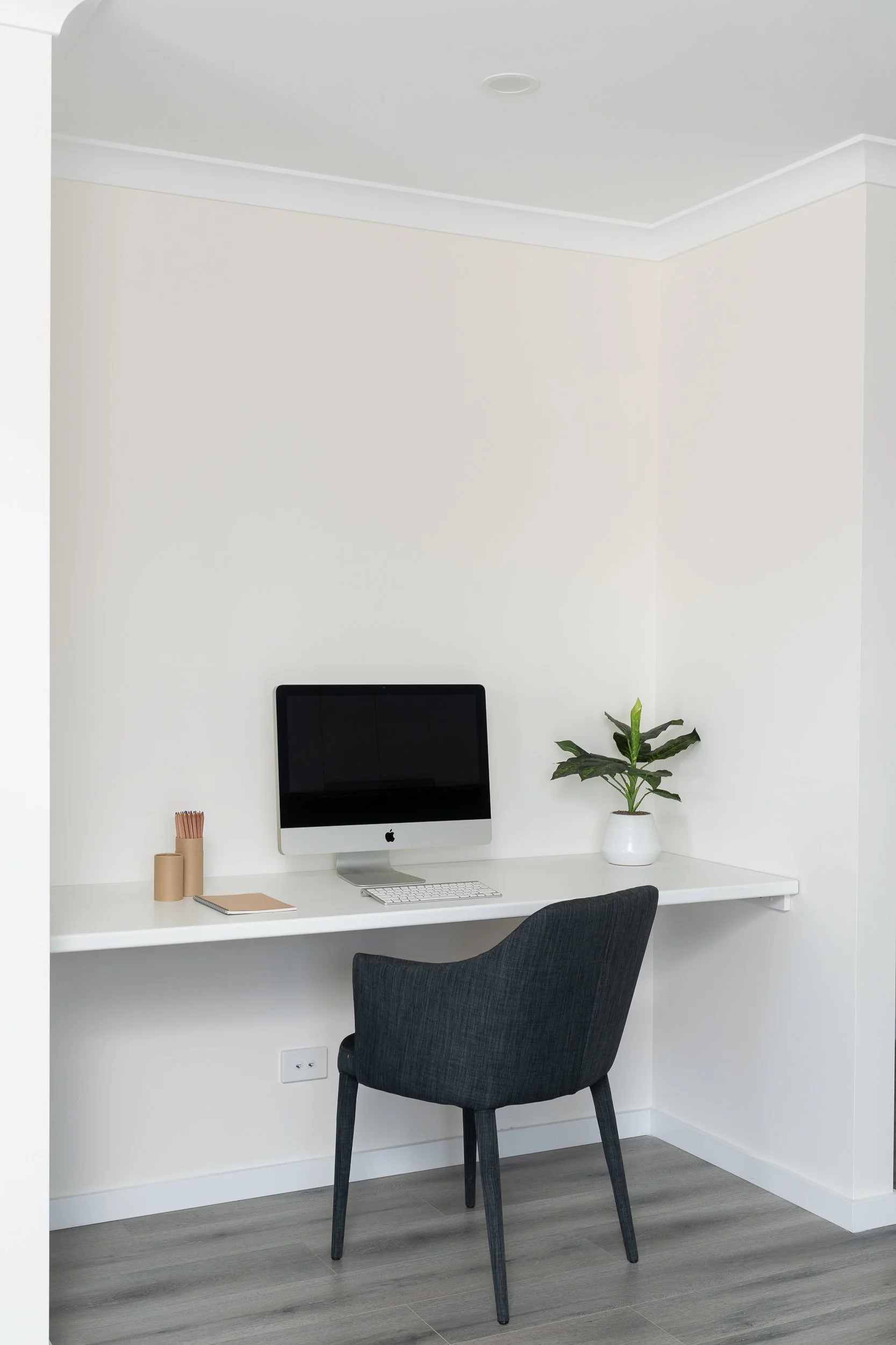 Minimalist workspace with a computer, keyboard, plant, and chair on a white desk.