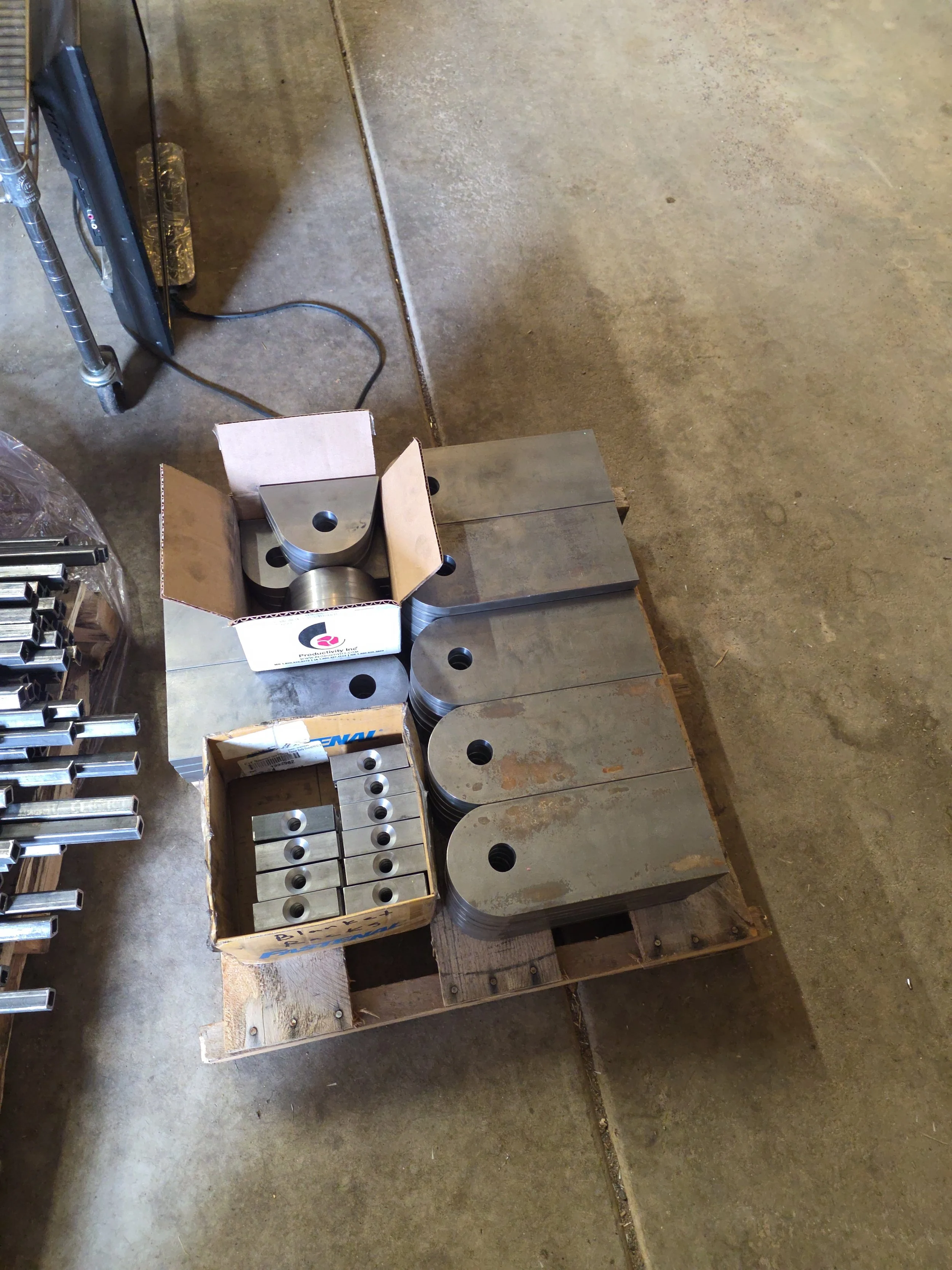 Various metal machine parts and components stored on a wooden pallet and in cardboard boxes in a workshop or warehouse setting.
