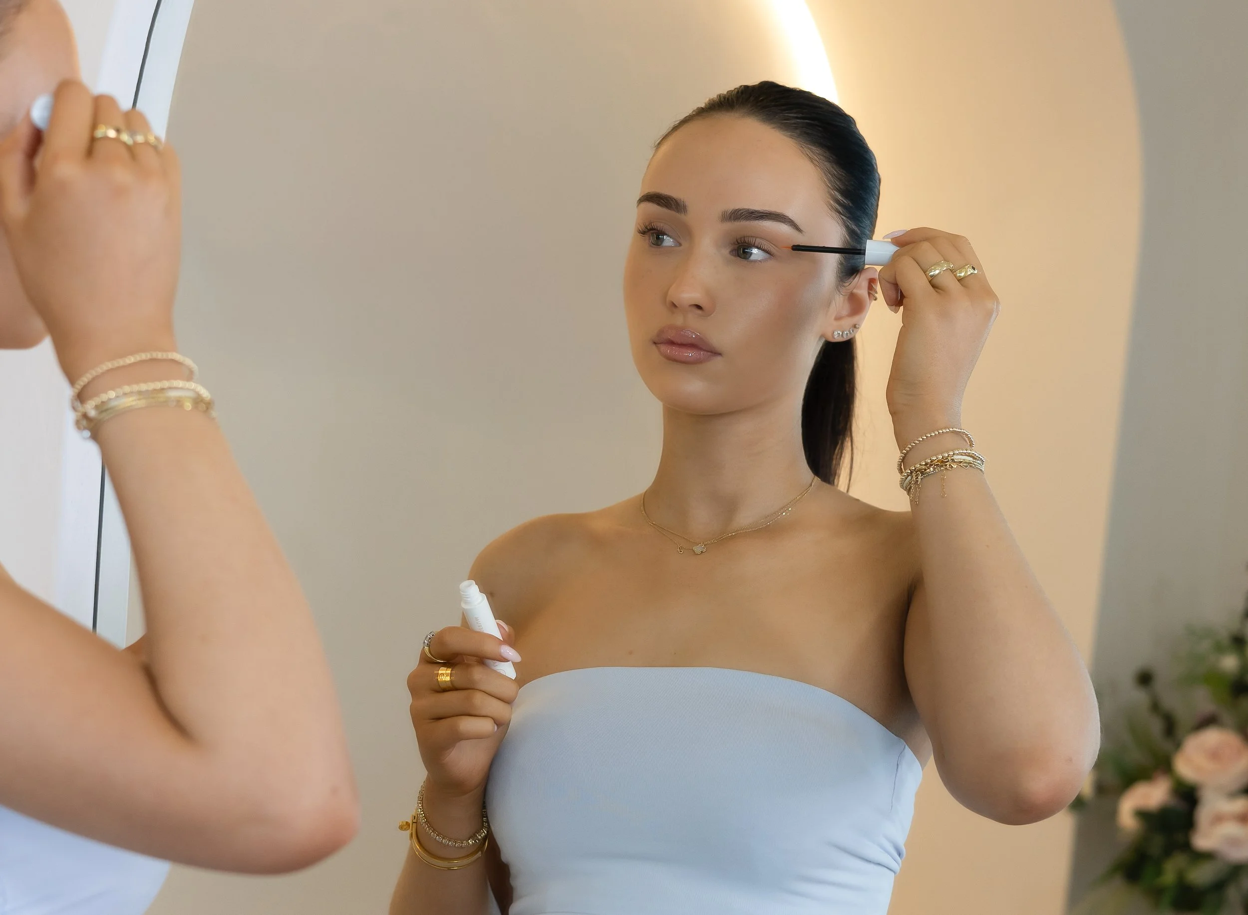 Woman applying Reform Cosmetics Lash Growth Serum in front of a mirror.