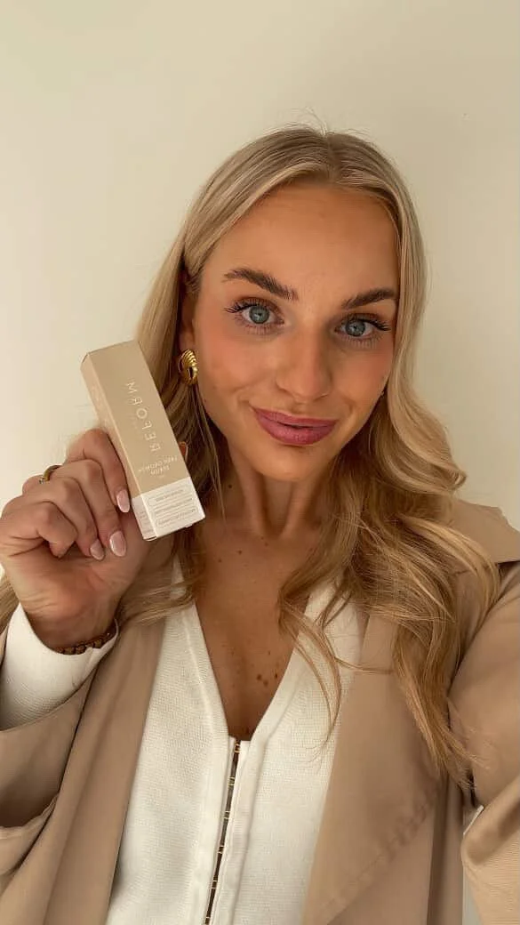 Girl holding Reform Lash Serum product in her right hand, smiling at the camera.