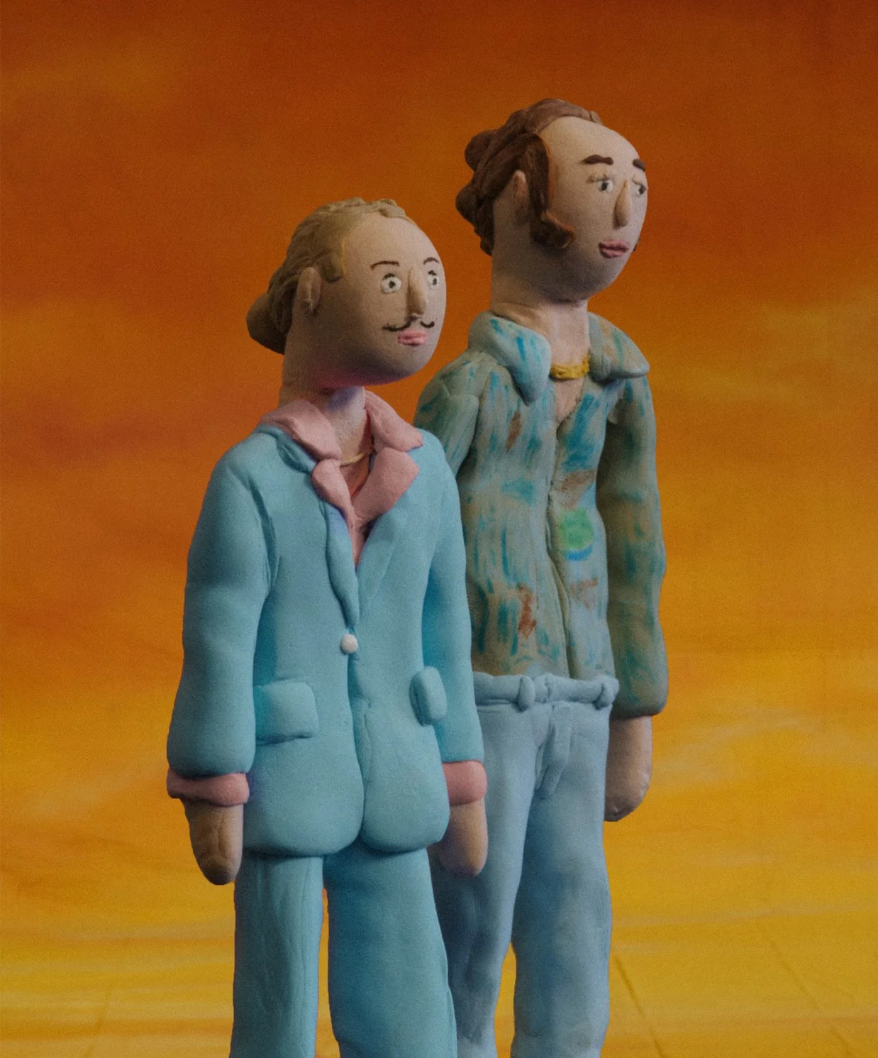 Two colorful clay sculptures of Baz and Wilder - standing against a sunset backdrop background.