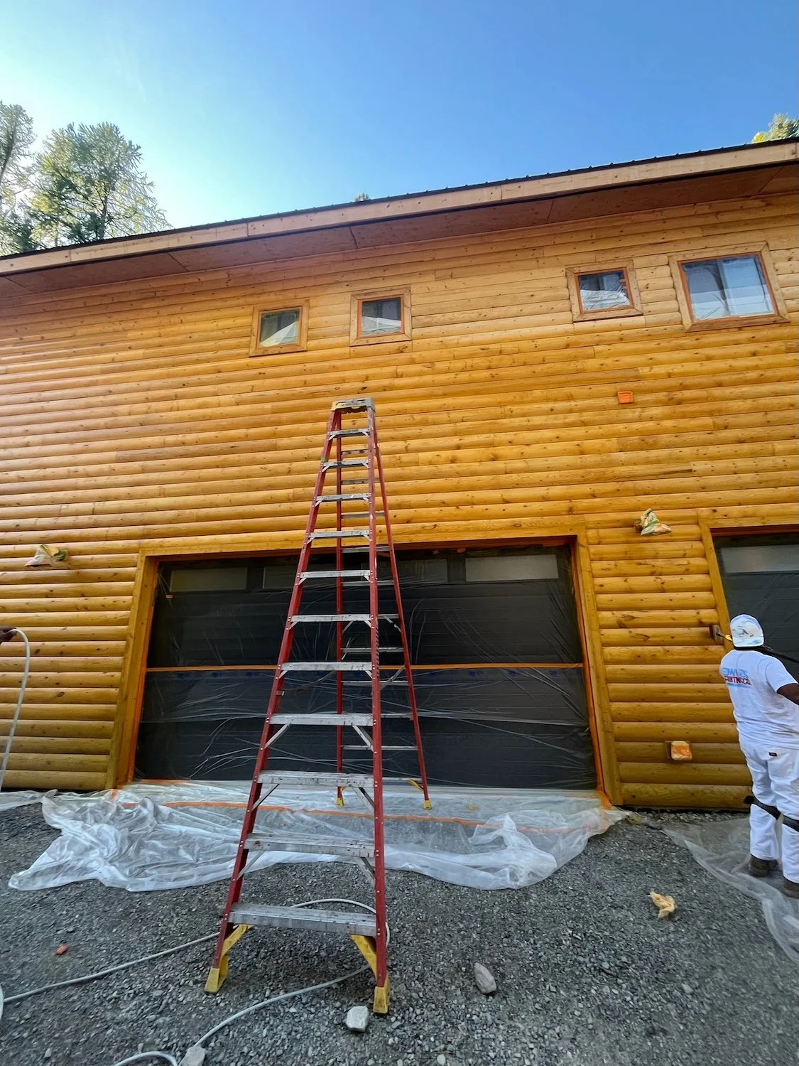 exterior log home stain with ladder and crew working