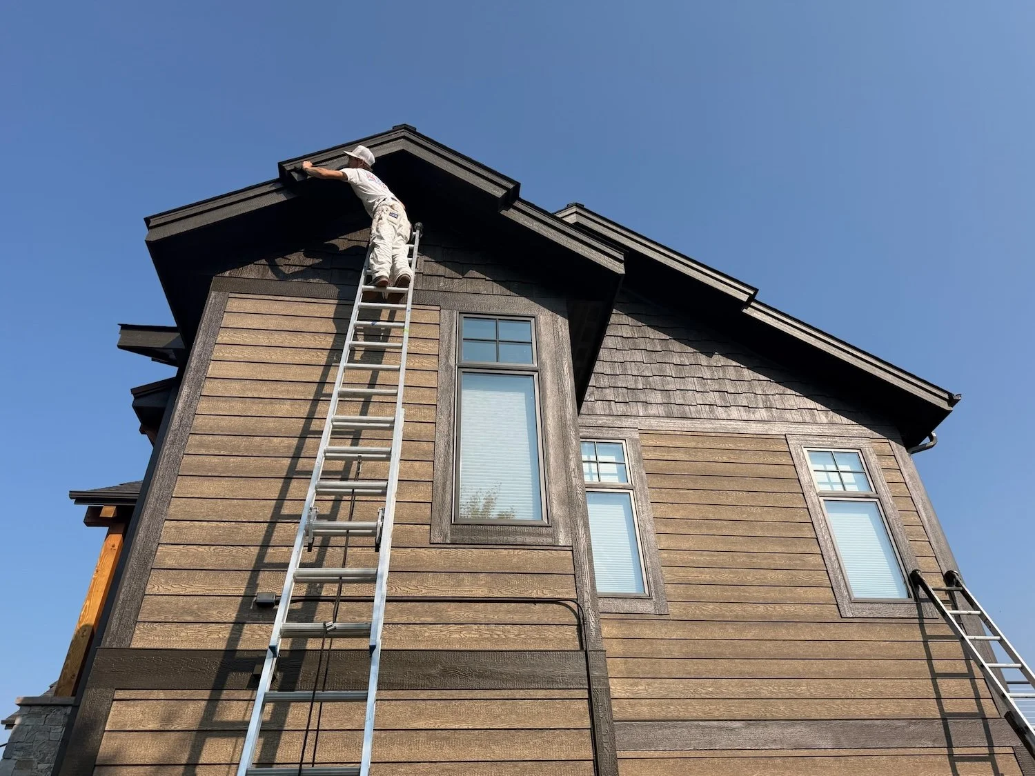 Edwards Painting Company employee on a ladder painting the second story exterior of a home in Flathead Valley