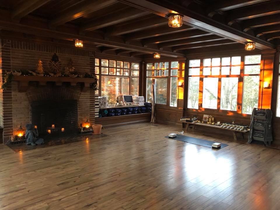 Cozy room with wooden floors and ceiling, large windows, a brick fireplace, candles, and a yoga mat on the floor.
