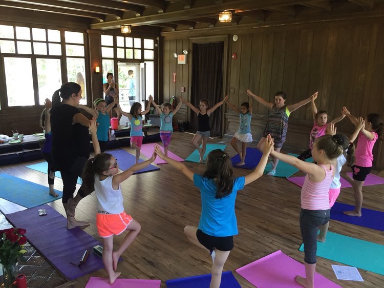 Children practicing yoga in a circle with an instructor on colorful mats in a wooden-floored studio.