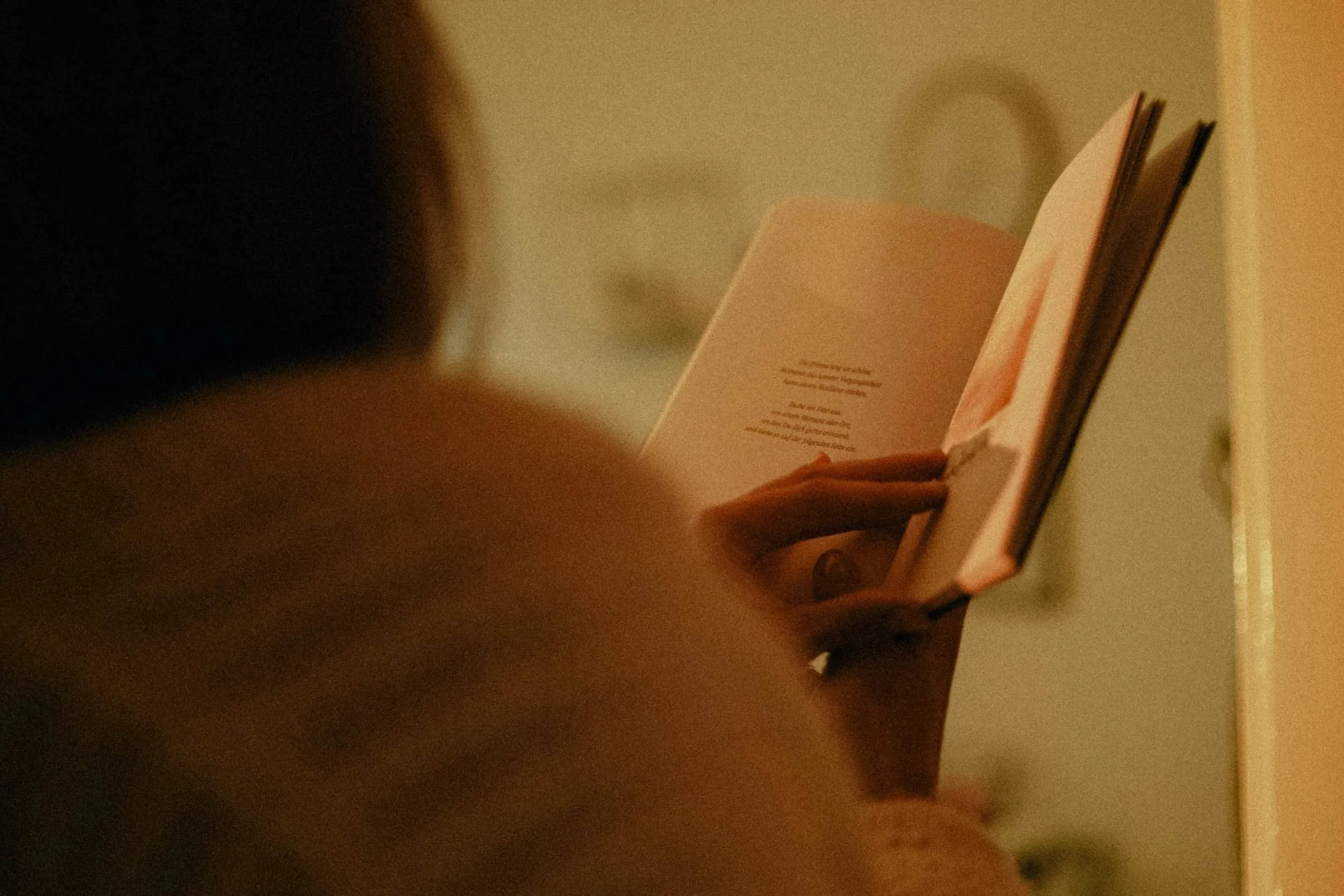 A person reads a therapy book in warm, soft lighting, with only their hand and part of the book visible.