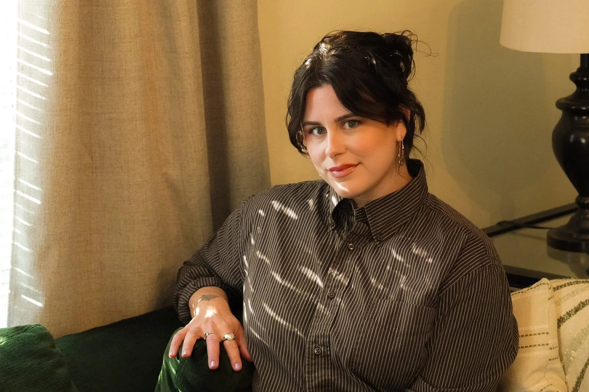 Therapist Emma Love sits on green couch in next to a window.