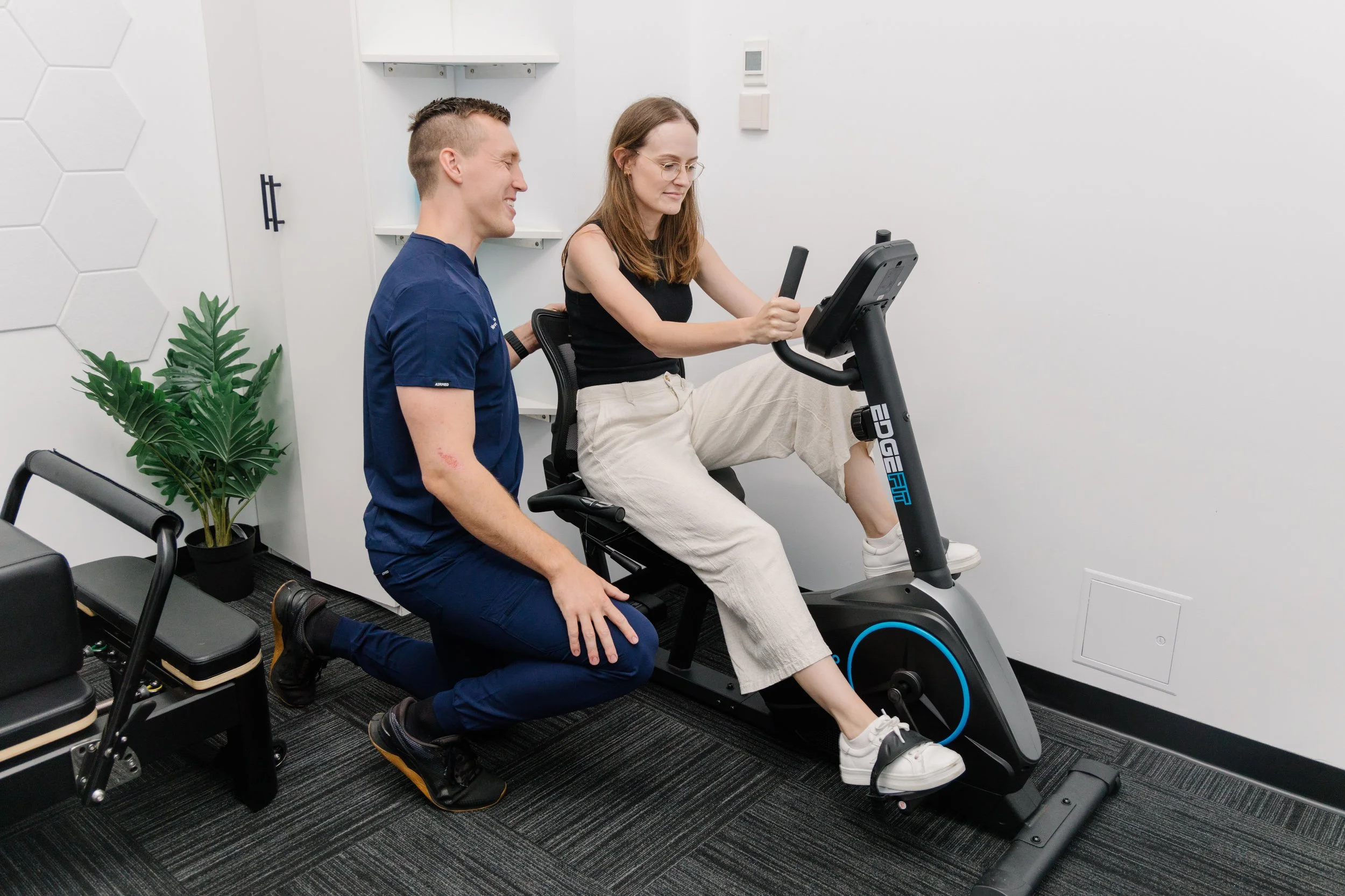 Physiotherapist supervising a patient on an exercise bike during rehabilitation at Move Right Physio Dakabin