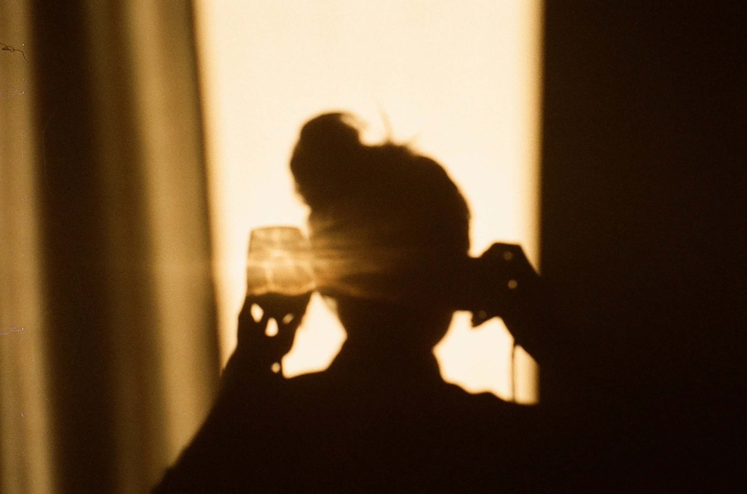 Silhouette of a person with a bun hairstyle holding a glass near their face against a bright background.